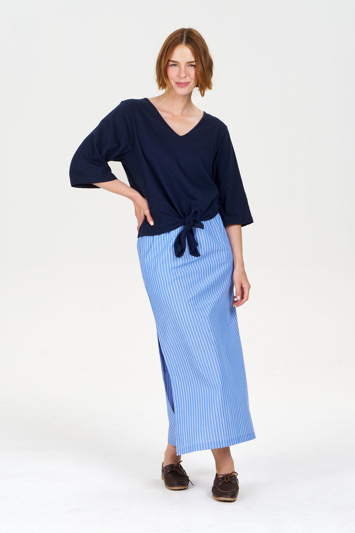 Woman wearing a navy organic cotton top and light blue striped skirt on a white background