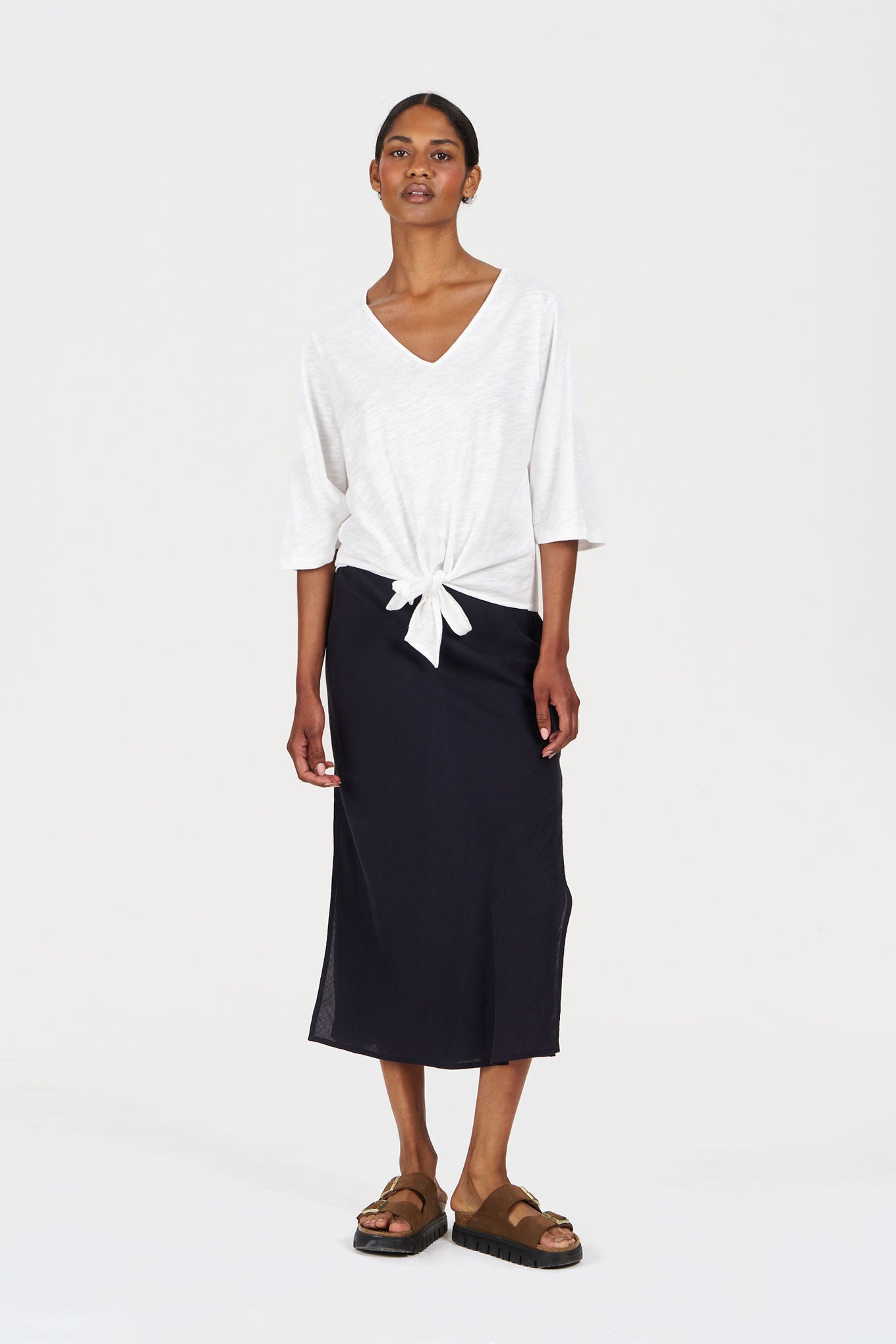 Woman wearing a white v neck top with knot detail paired with a black long skirt and sandals