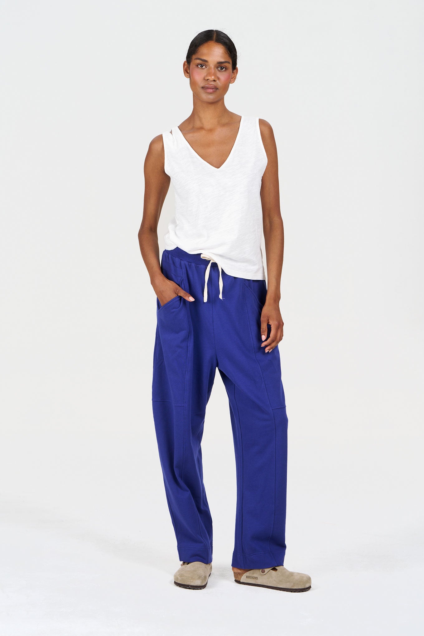 Woman wearing a white sleeveless top and blue pants on a white background