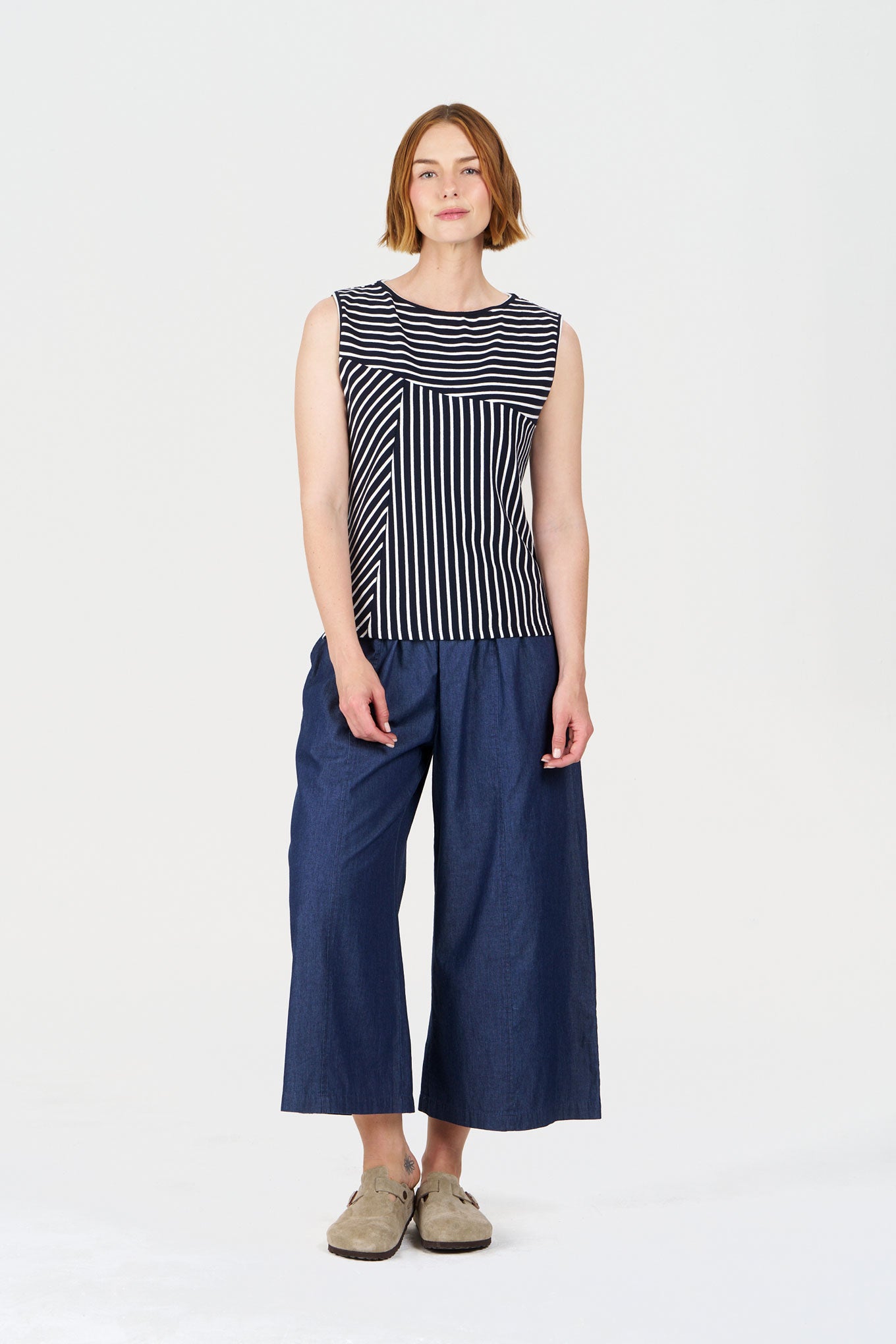 Woman wearing a sleeveless striped top and wide-leg pants on a white background