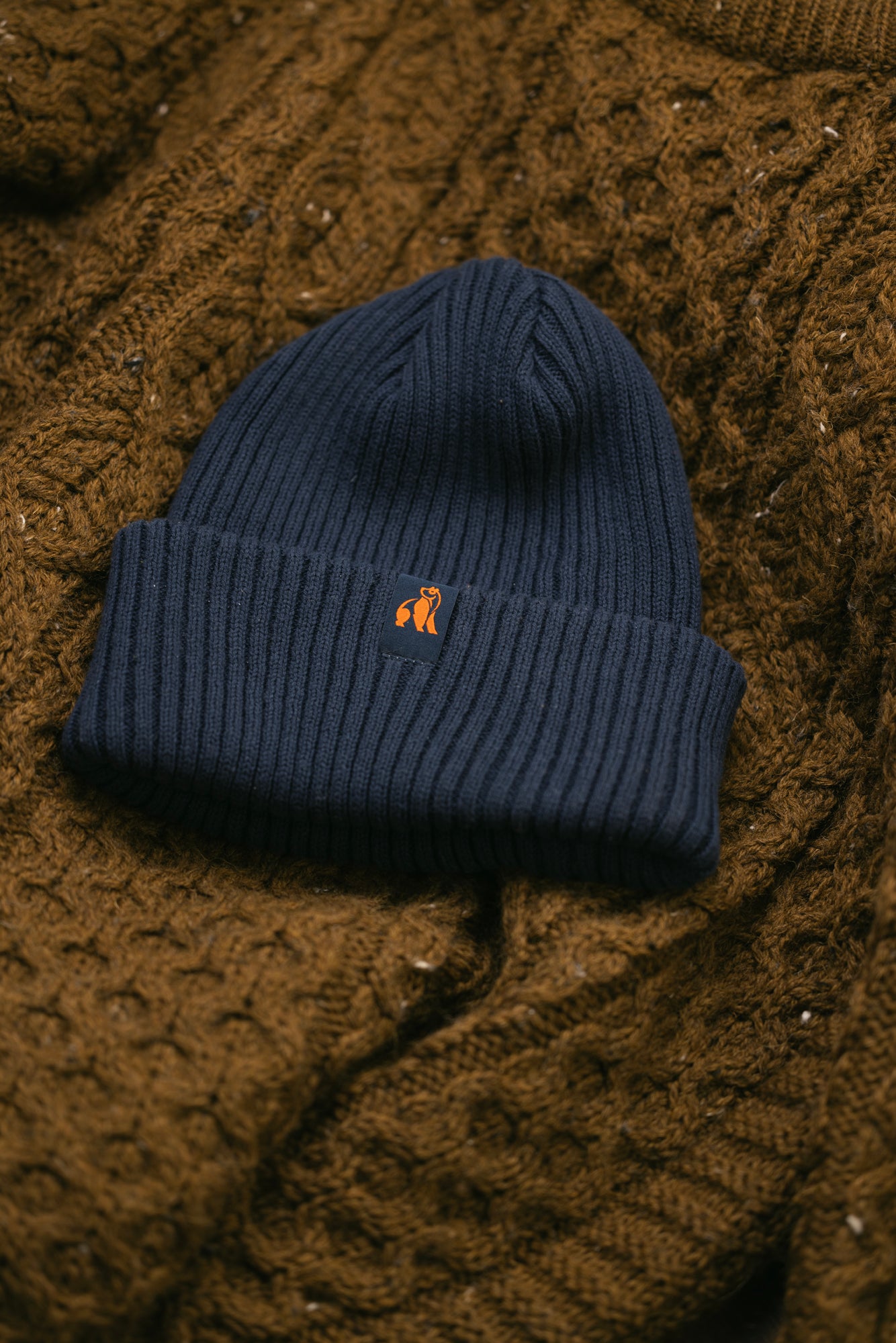 A navy blue ribbed Swole Panda beanie resting on a brown textured organic cotton sweater.
