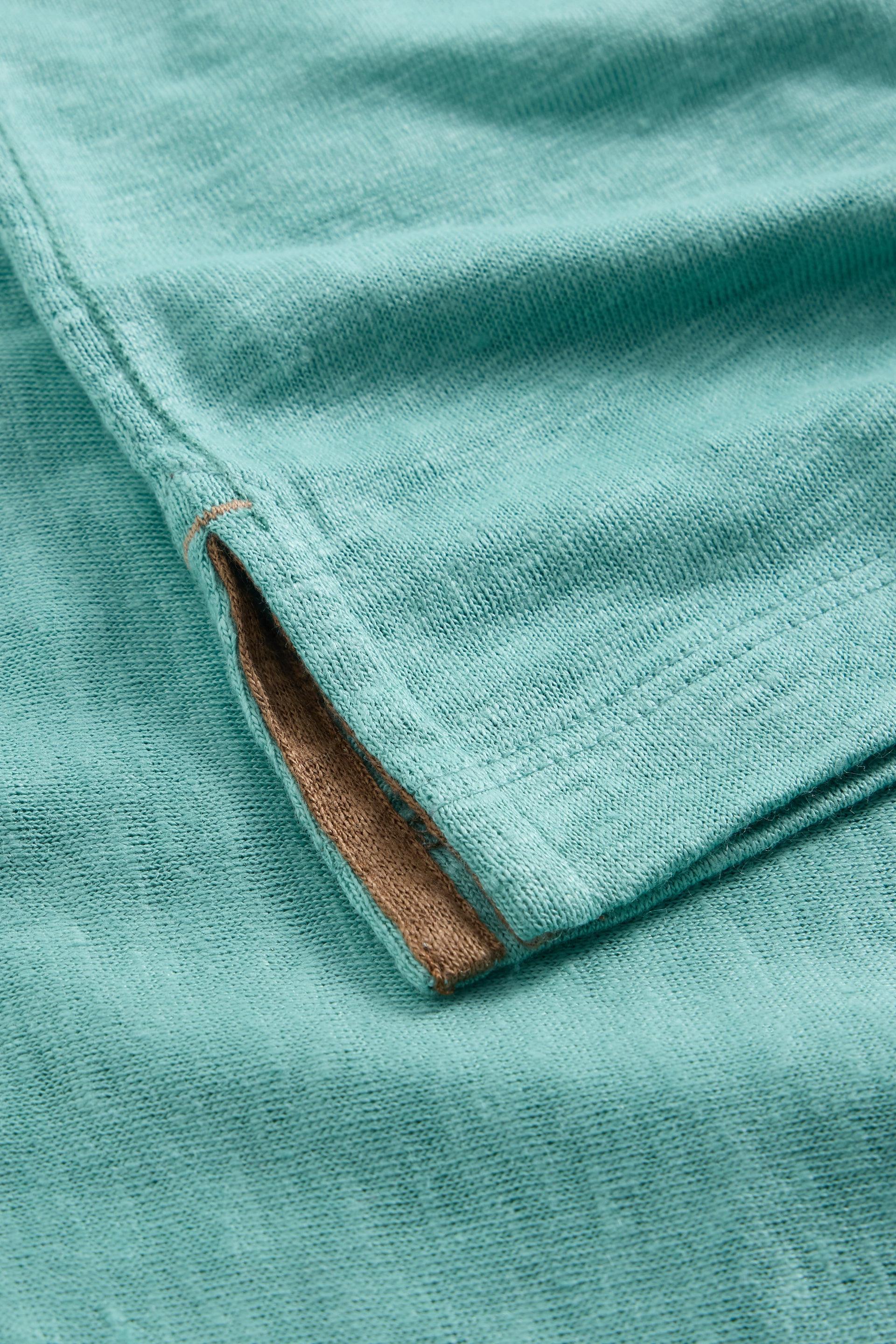 Close-up of a teal mens linen t-shirt sleeve cuff showing the textured fabric and inner contrast lining.