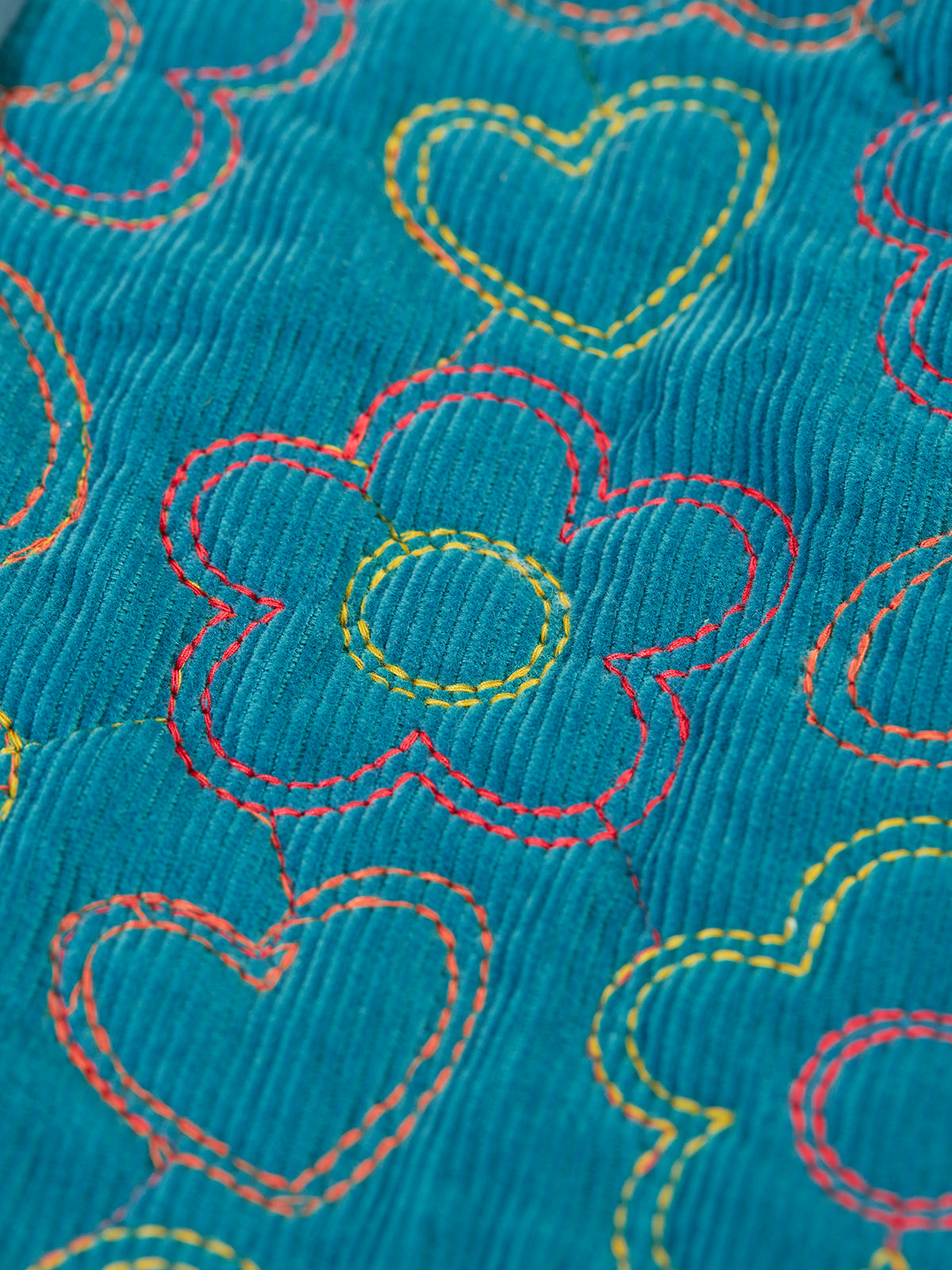 Close-up of teal organic cotton corduroy fabric featuring colorful stitched flower and heart patterns.