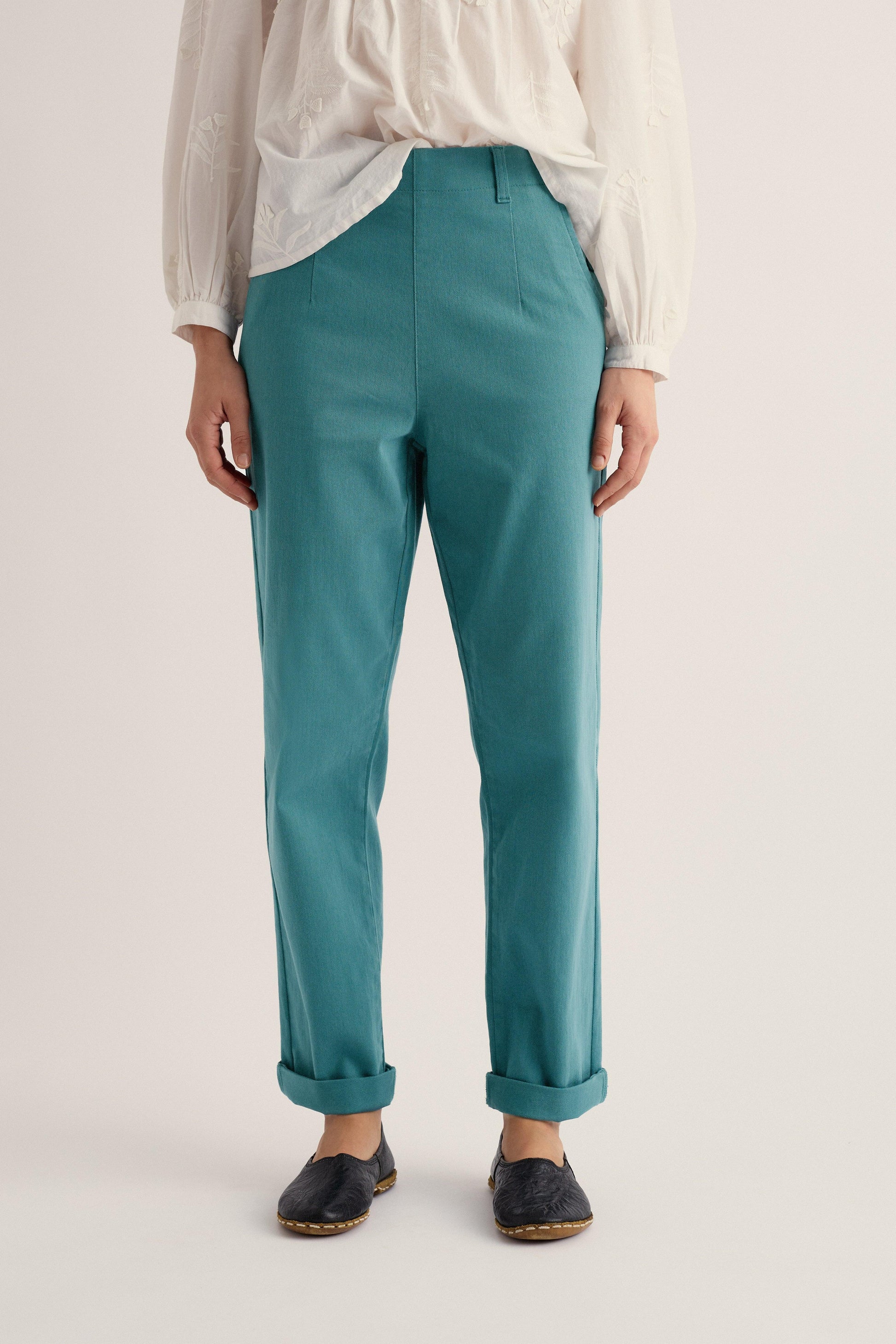 Person wearing teal pants and a white shirt on a light background