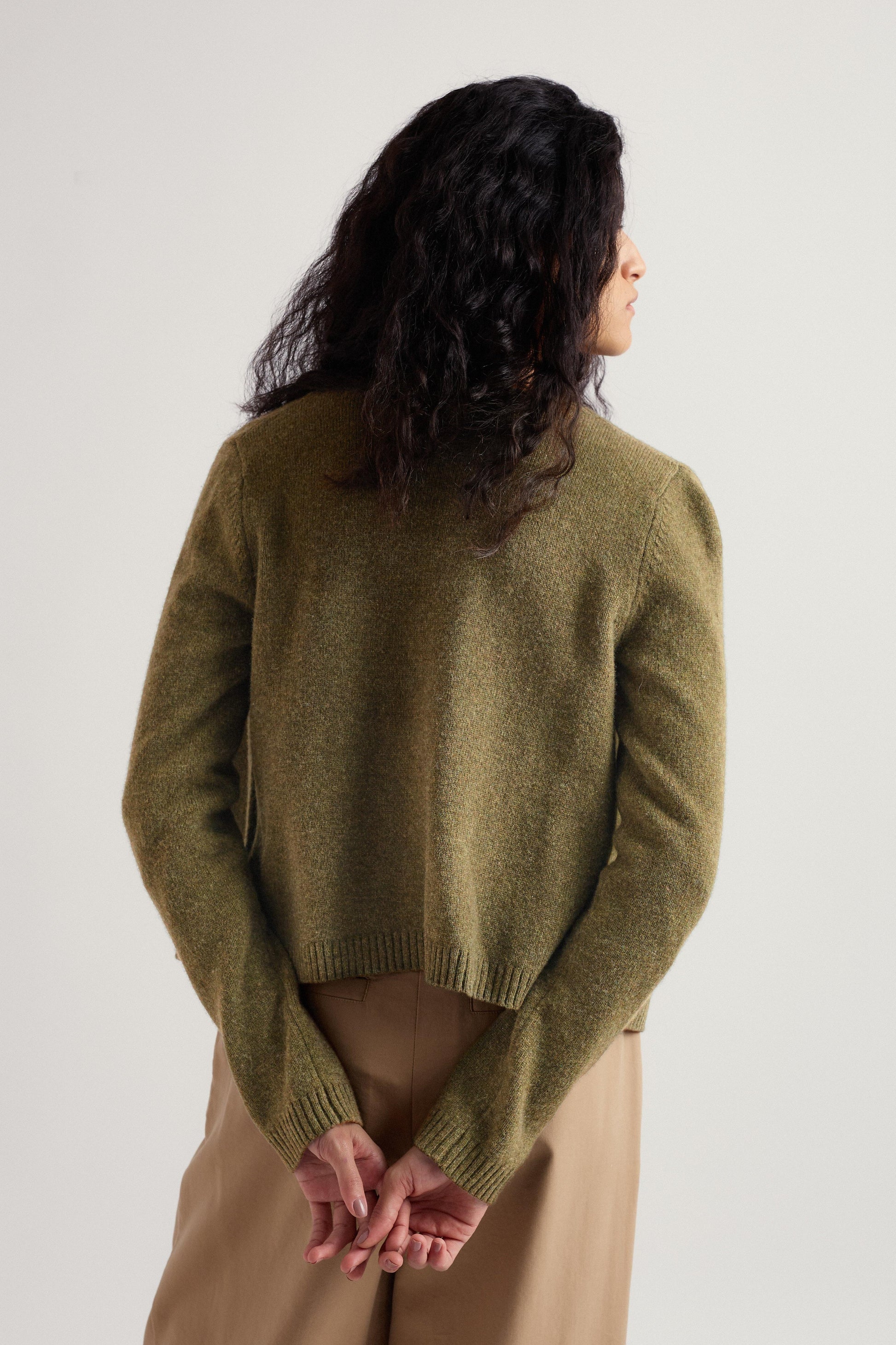 Person wearing a green merino wool cardigan and beige pants against a white background