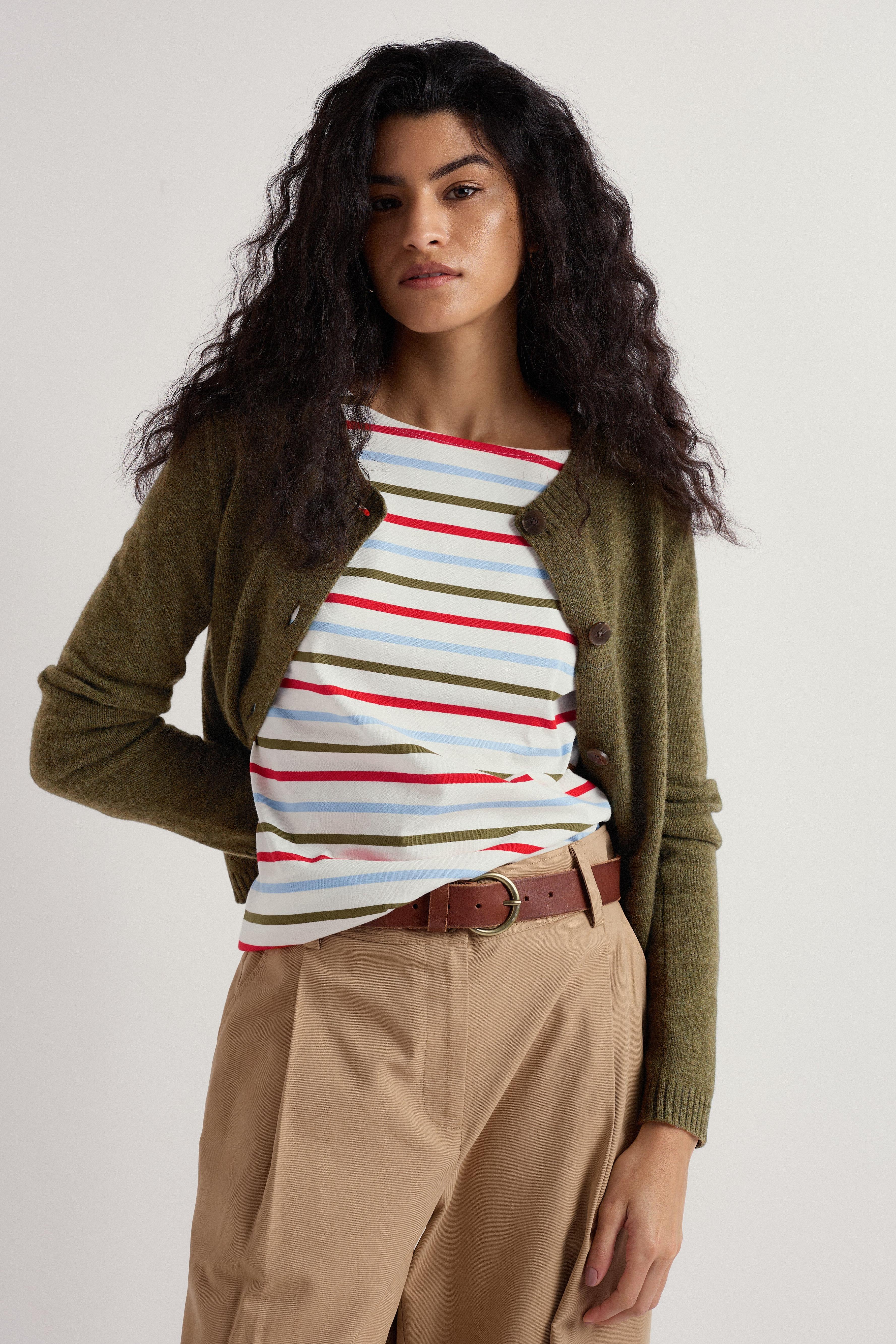 Woman wearing a striped top, green merino wool cardigan, and beige pants on a plain background