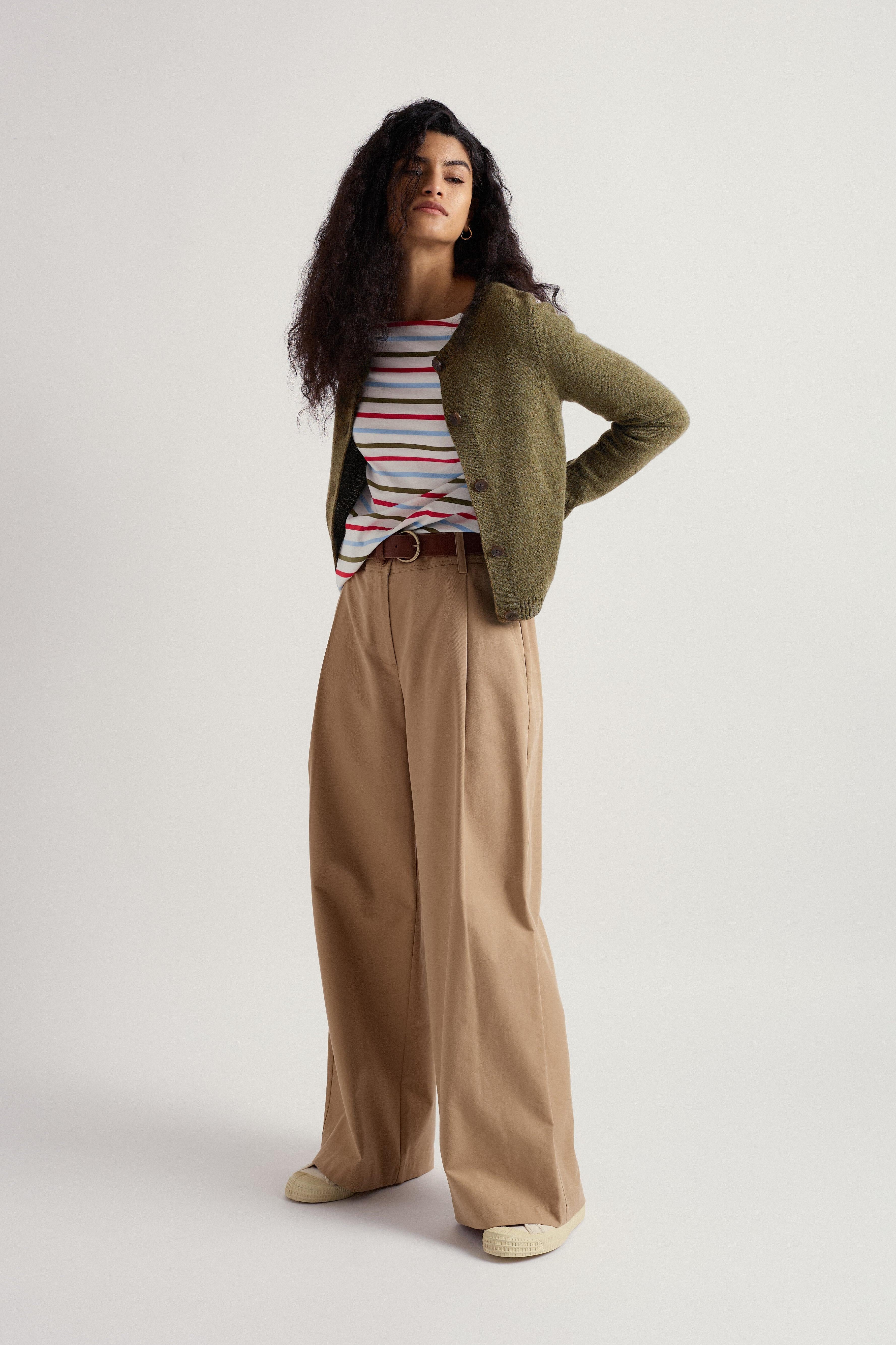 Woman wearing a striped shirt, green cardigan, and beige pants on a white background