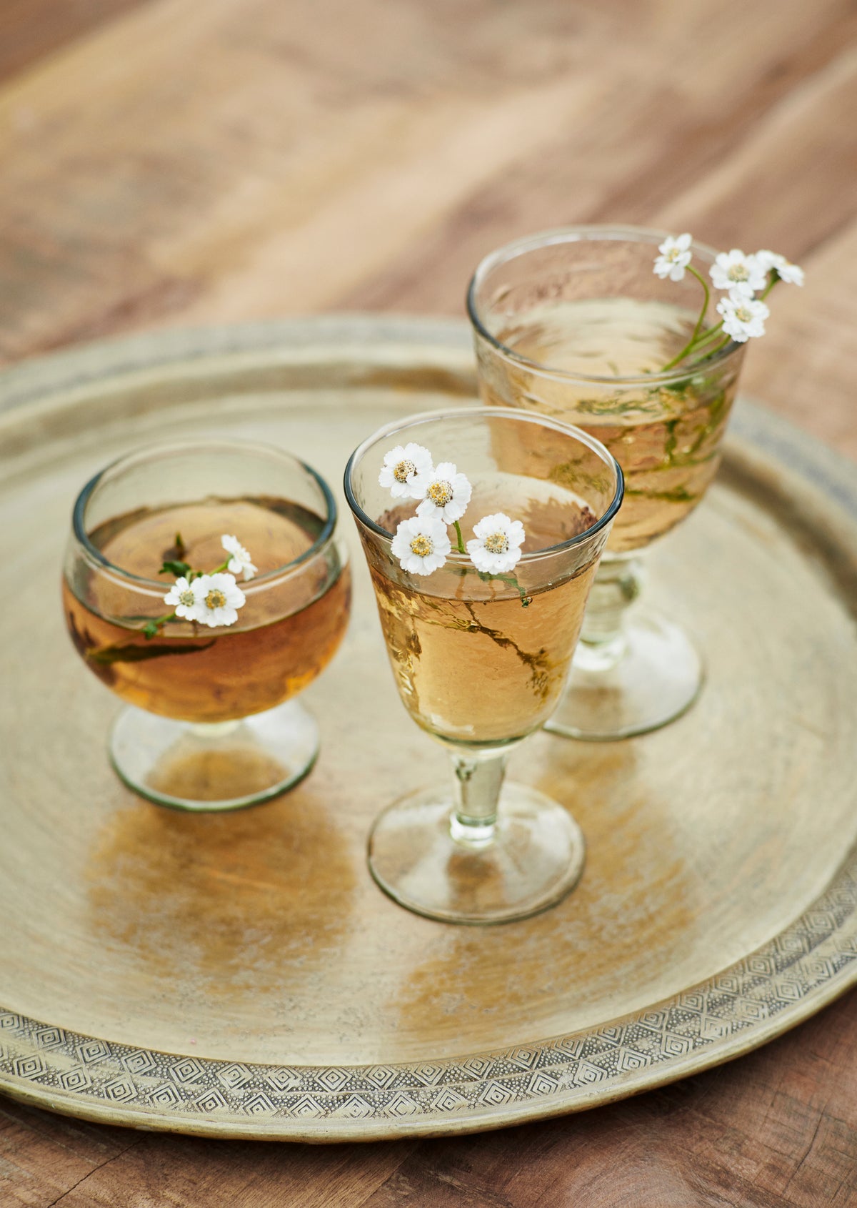 Two clear textured wine glasses with small white flowers on a brass tray