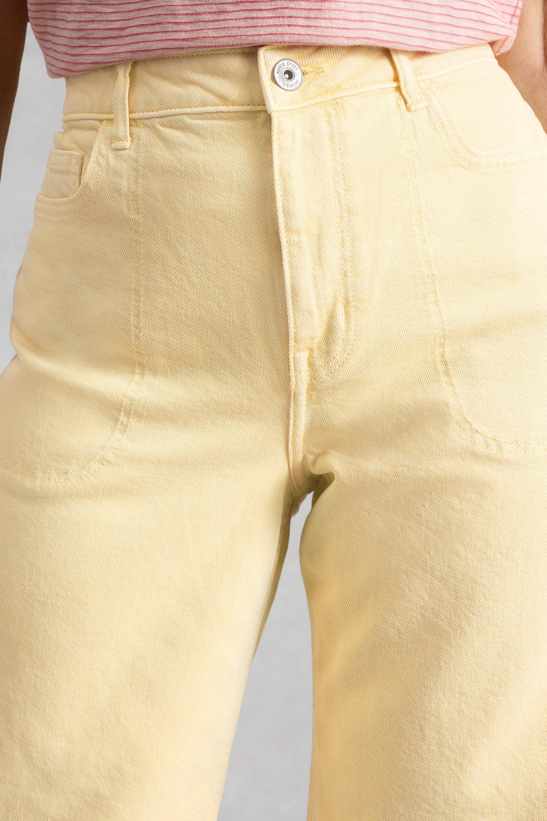 Close-up of light yellow organic cotton jeans with a button on a neutral background