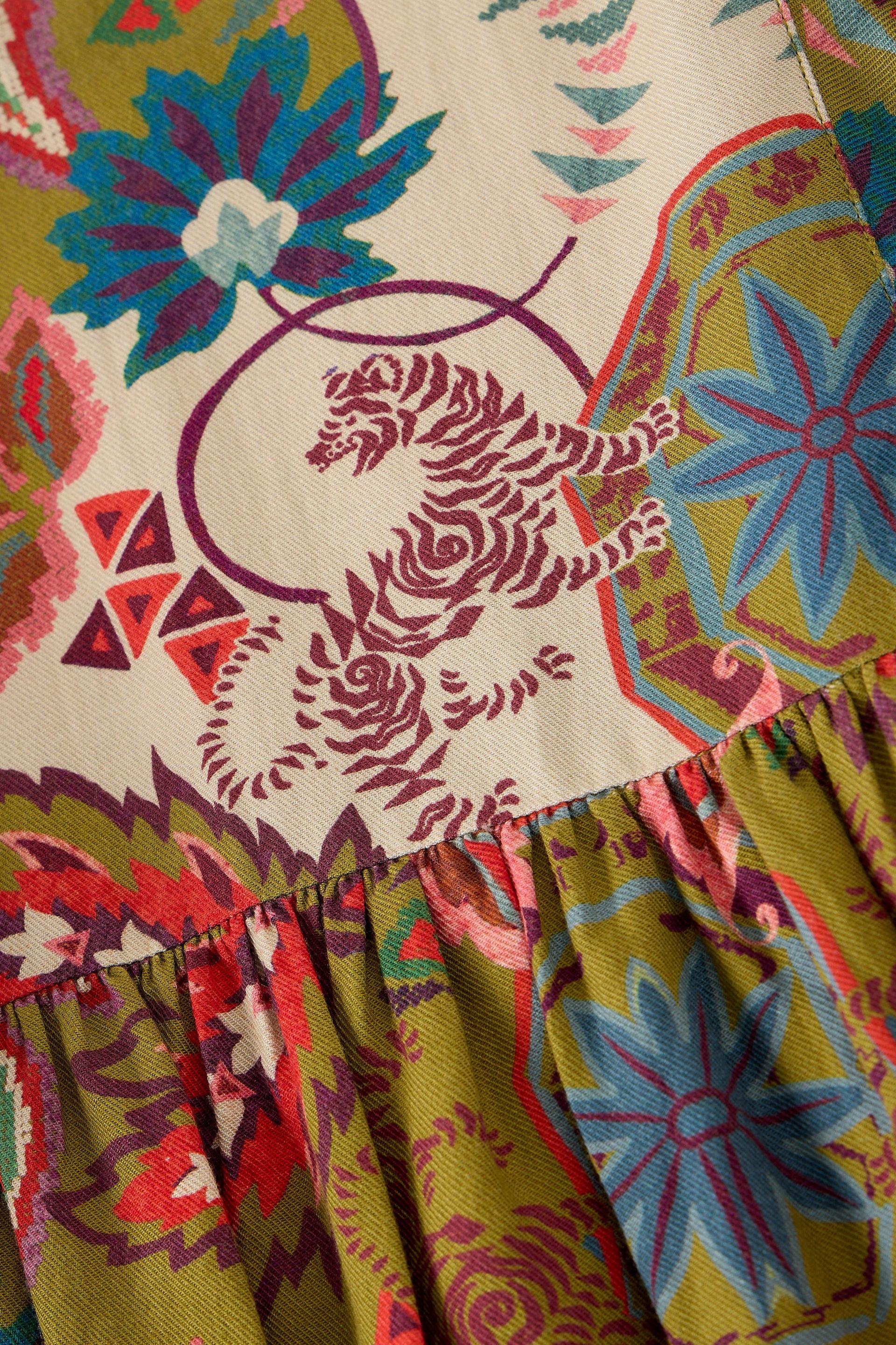 Close-up of a patterned garment showing a cream base with a burgundy tiger motif and multicolored floral and geometric prints in olive green, blue, pink, and red.