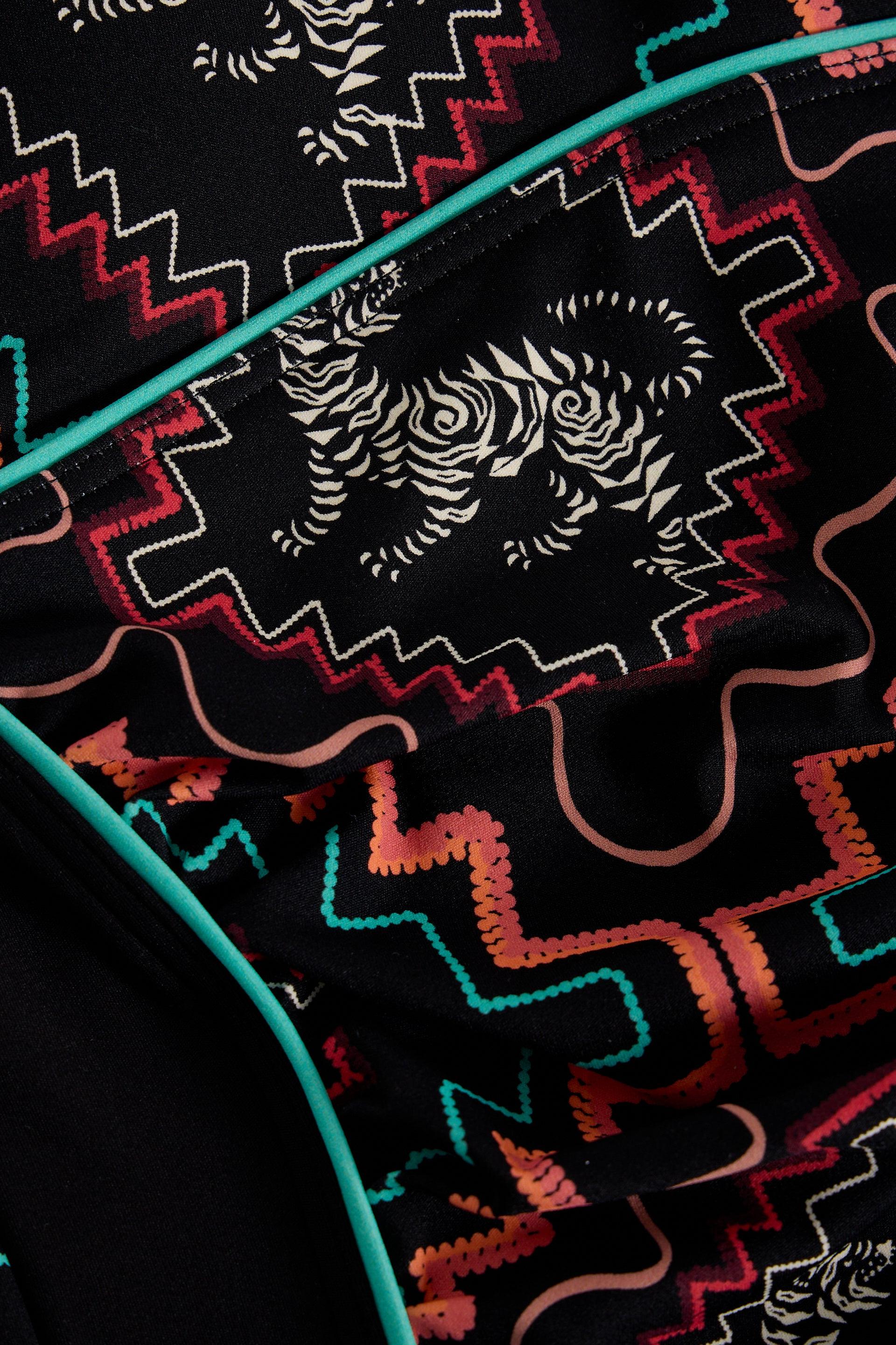 Close-up of black fabric featuring white tiger silhouettes, colorful zigzag patterns, and teal trim