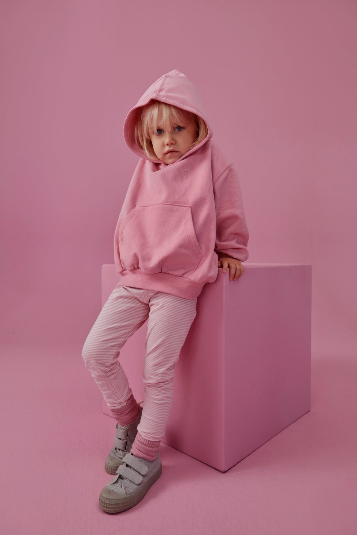Toddler wearing a pink Gray Label organic cotton hoodie leaning against a matching pink cube