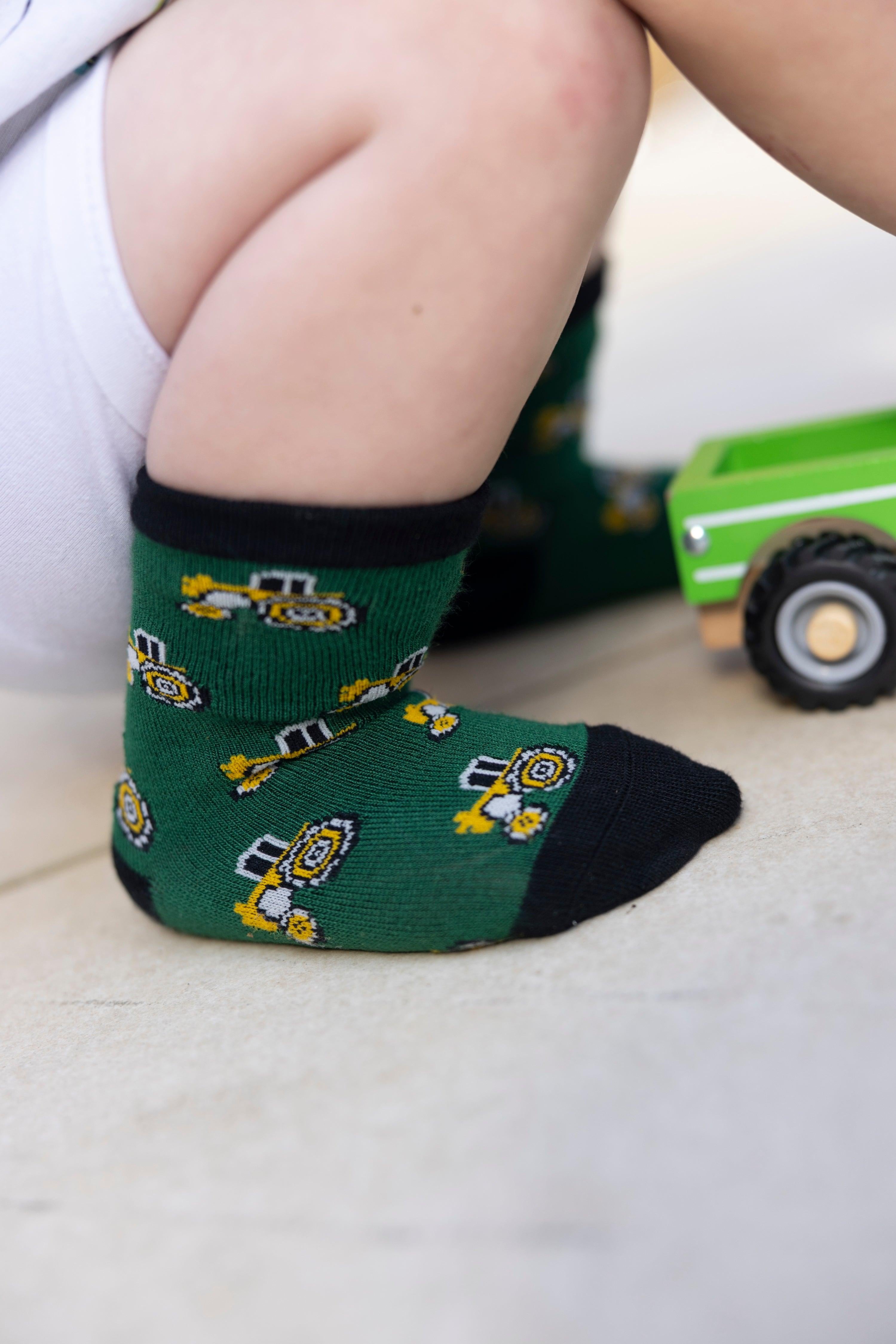 Close-up of a toddler wearing green construction-patterned socks while playing with a green toy truck on a floor.