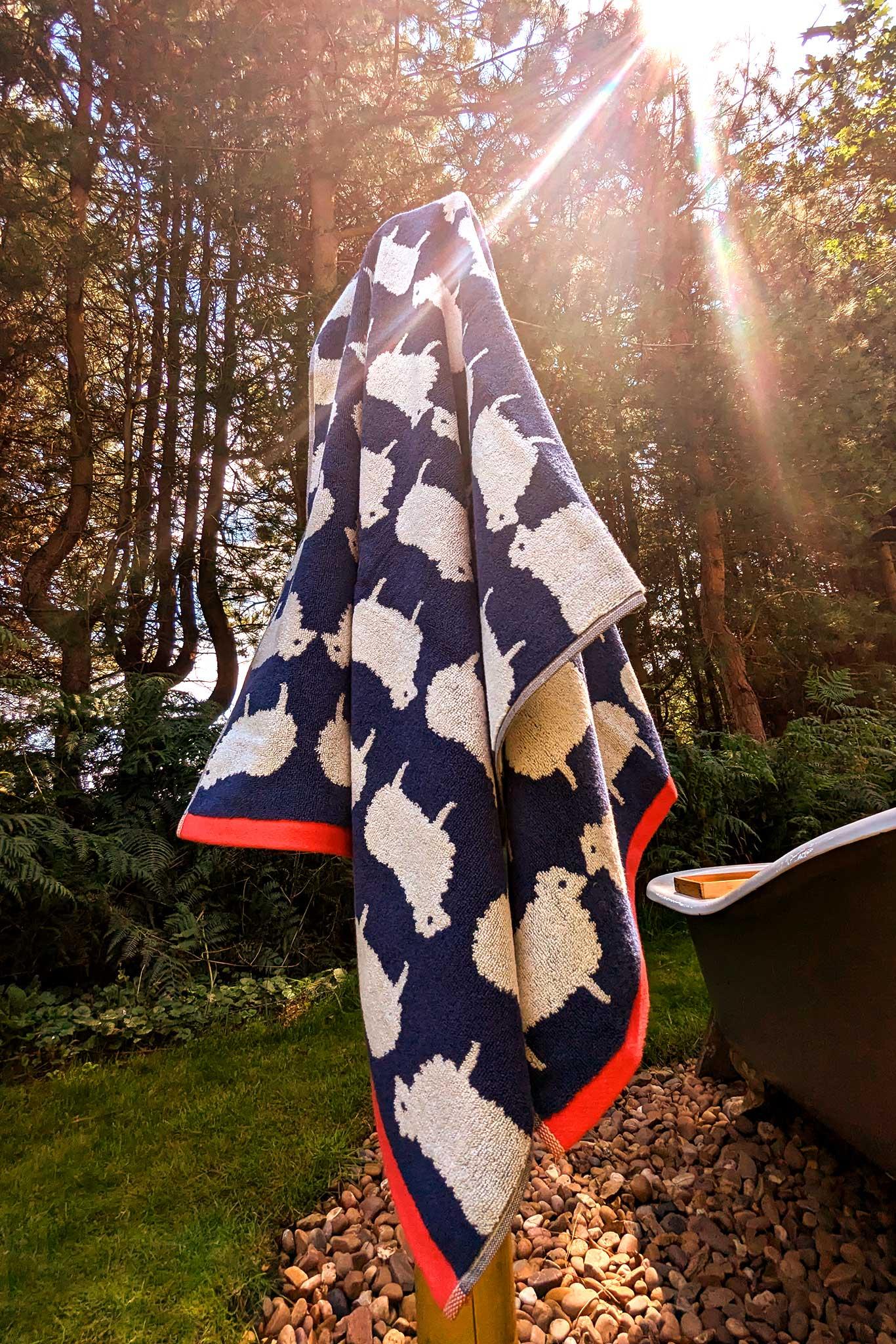 Navy organic cotton towel with white animal pattern draped over a garden bench with trees in the background
