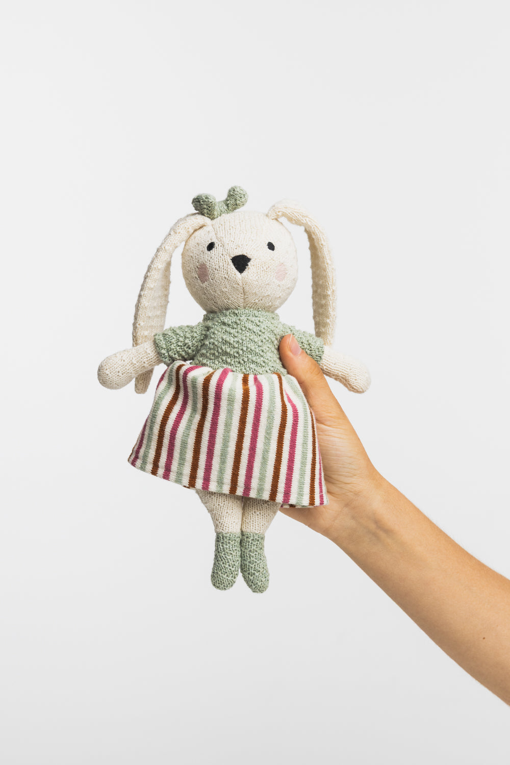 Hand holdng a bunny soft toy with colourful skirt on a white background
