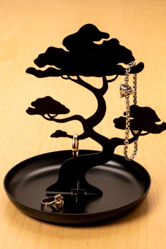 Black tree-shaped jewelry holder with rings on a wooden surface