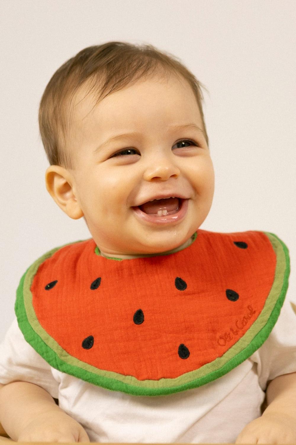 Baby wearing an organic cotton baby bib with fun watermelon design and smiling