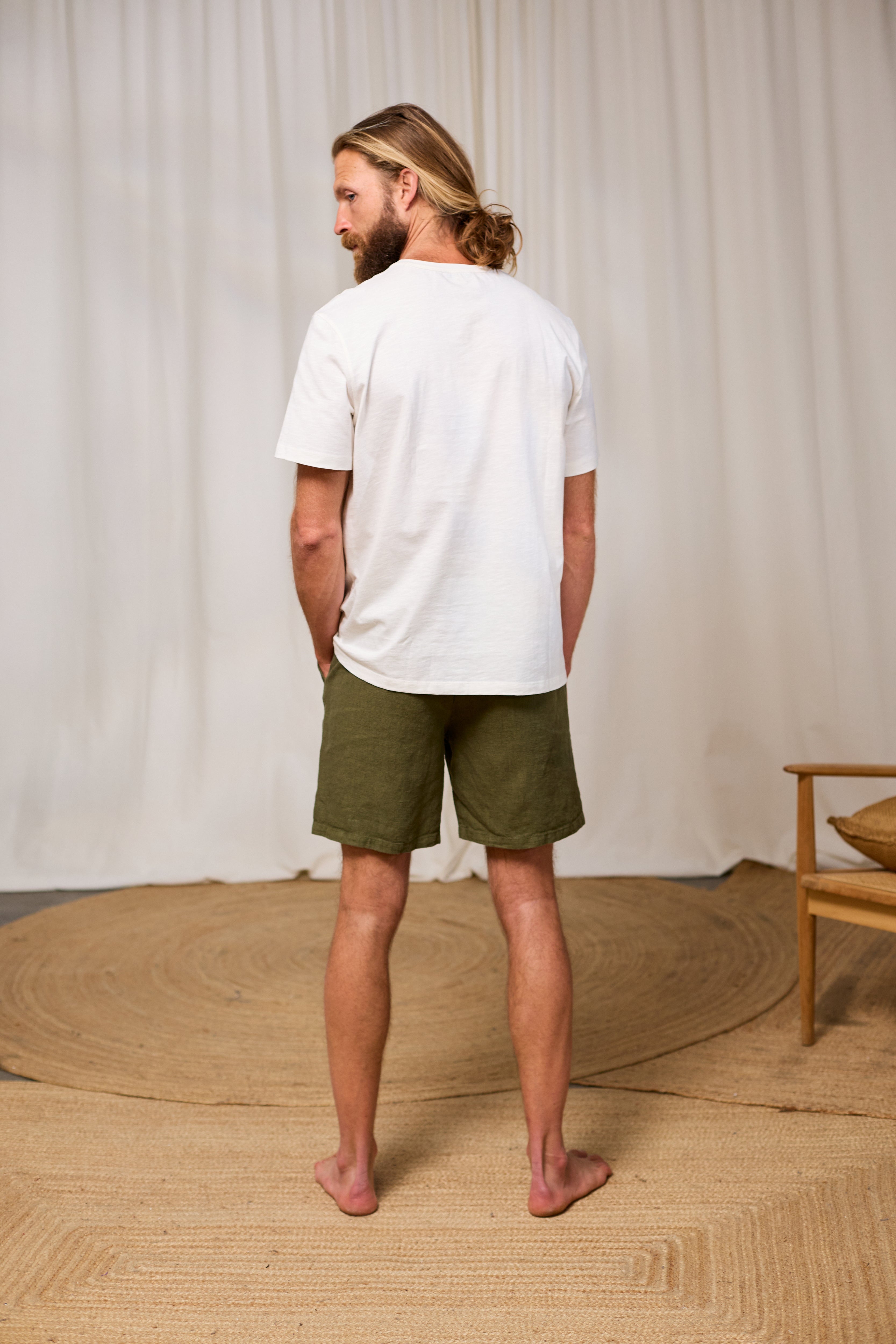 Man wearing a white organic cotton t-shirt and green shorts standing in a room with a neutral background.