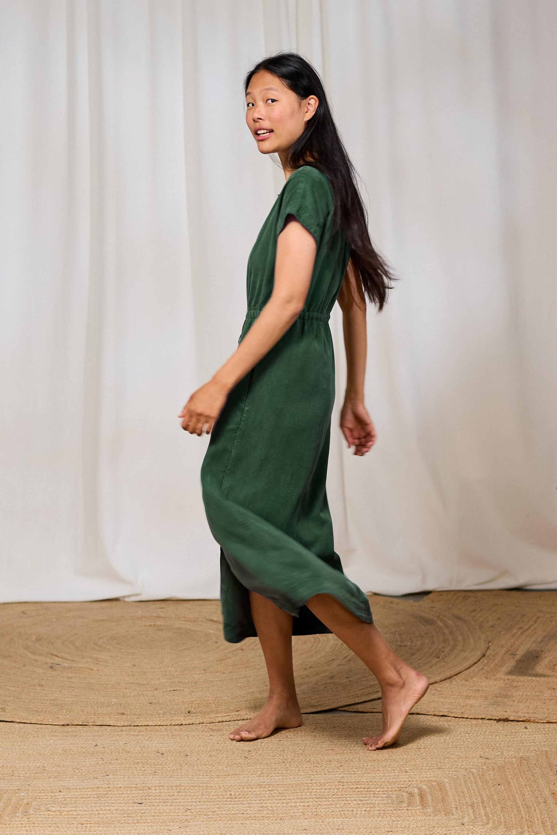 Woman in a green dress walking on a textured floor with a white curtain background
