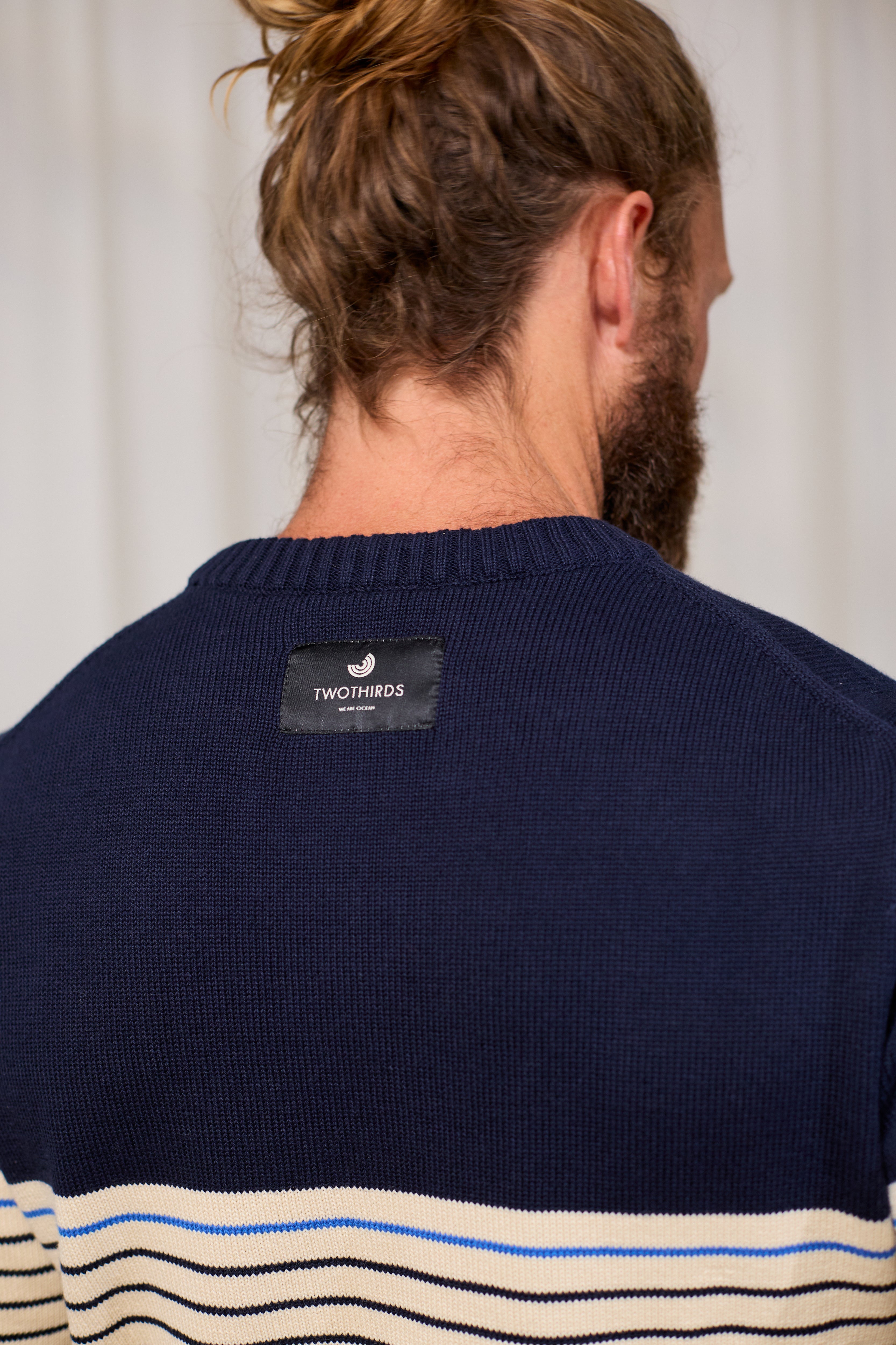 Person wearing a navy organic cotton knit sweater with a TWOTHIRDS label on the back, against a plain background