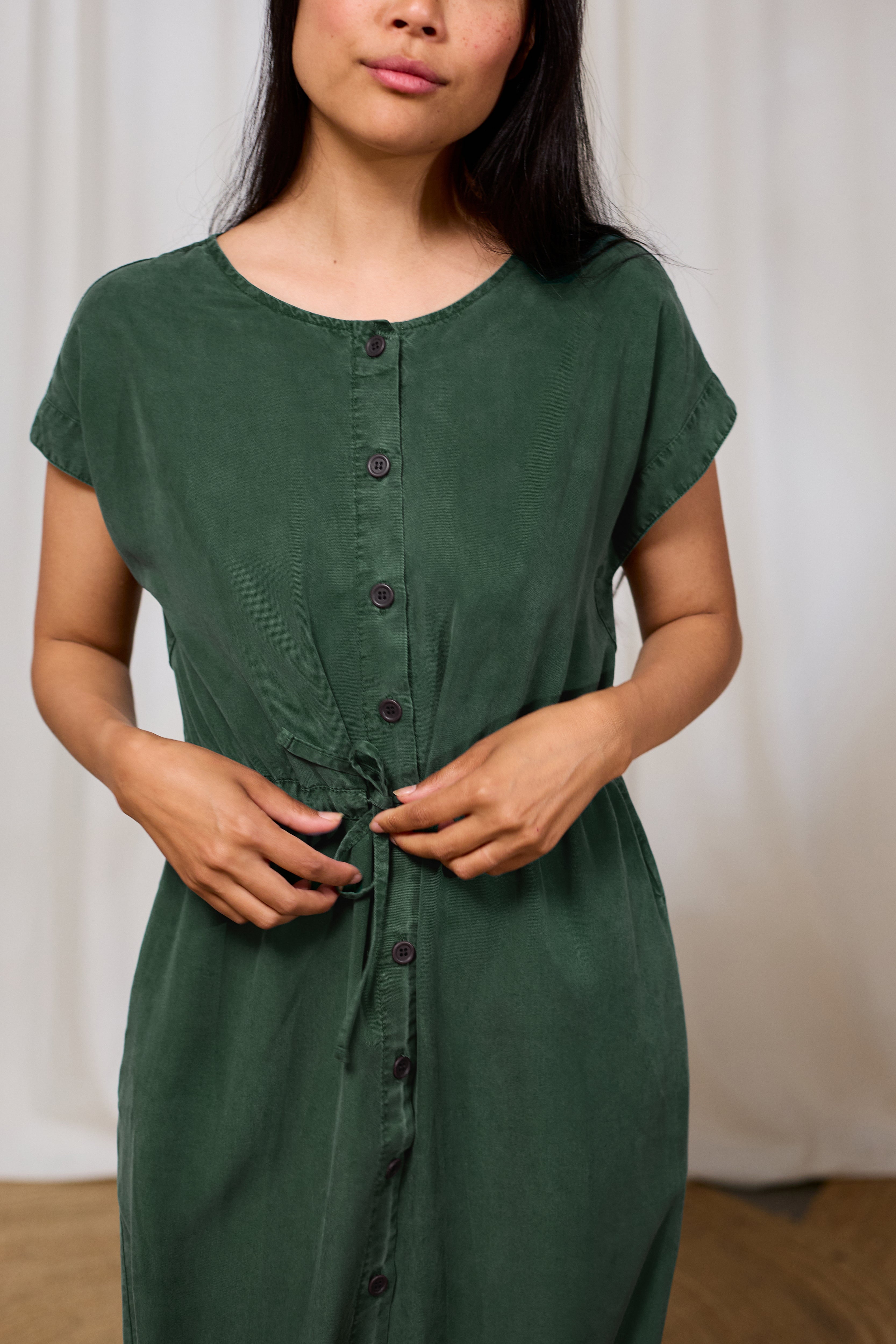Woman wearing a green summer dress with buttons against a white background