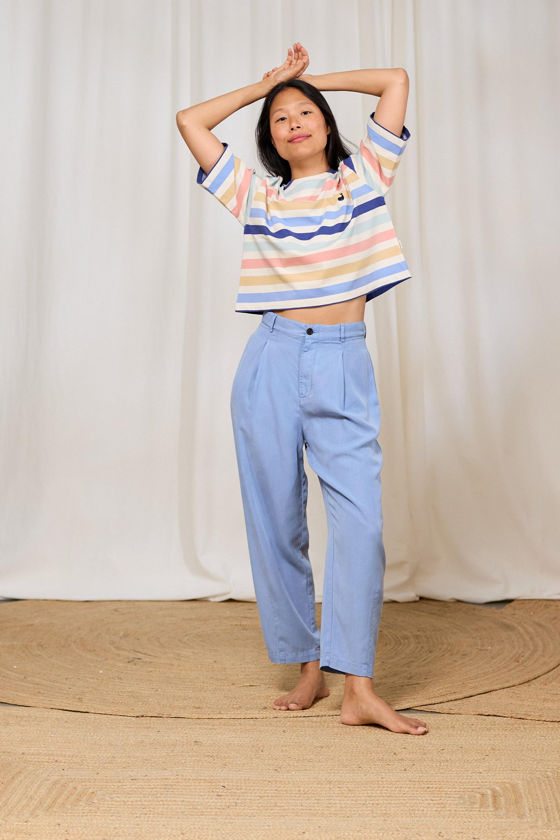 Person wearing a TWOTHIRDS striped t-shirt and light blue pants against a white curtain background
