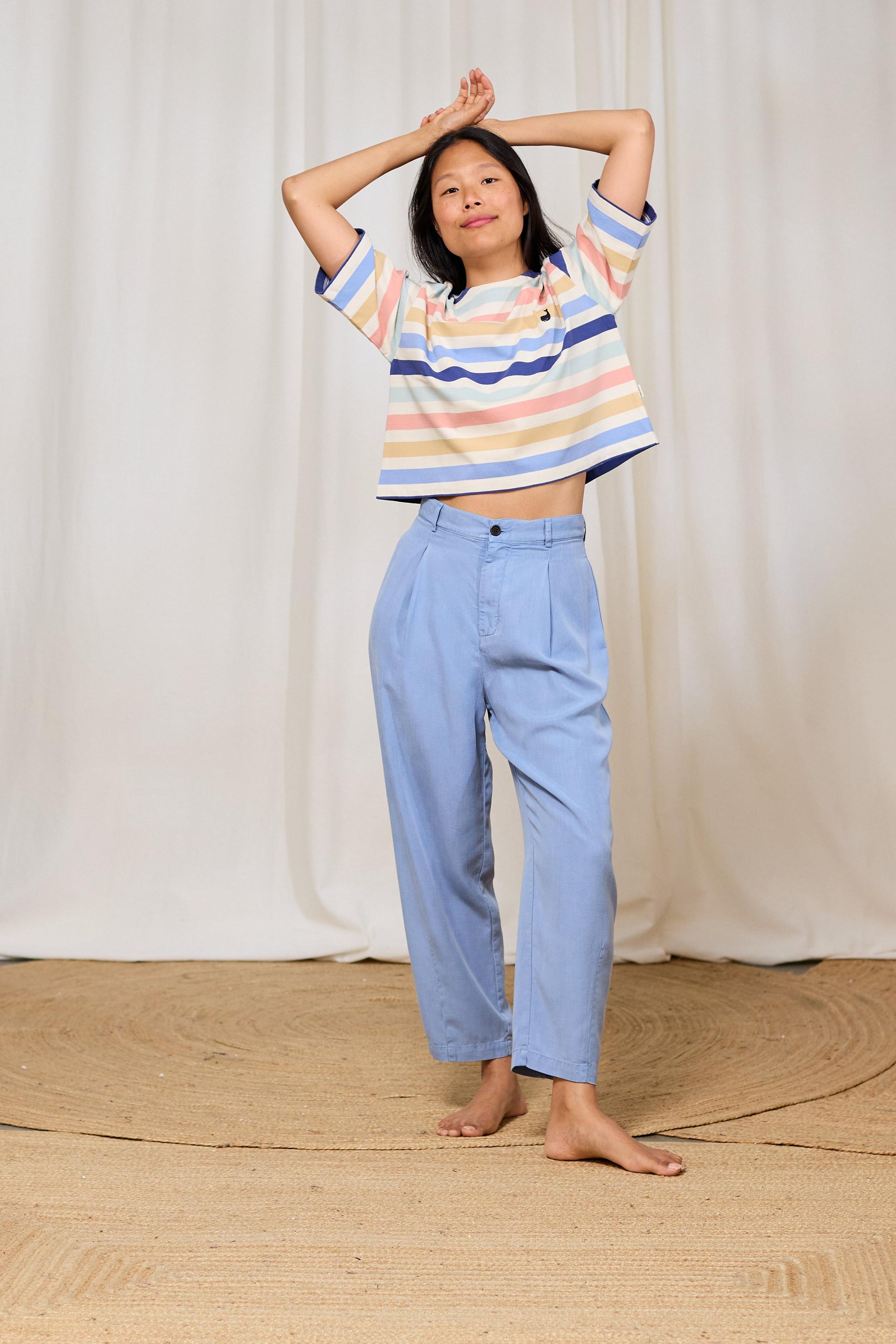 Person wearing a TWOTHIRDS striped t-shirt and light blue pants against a white curtain background