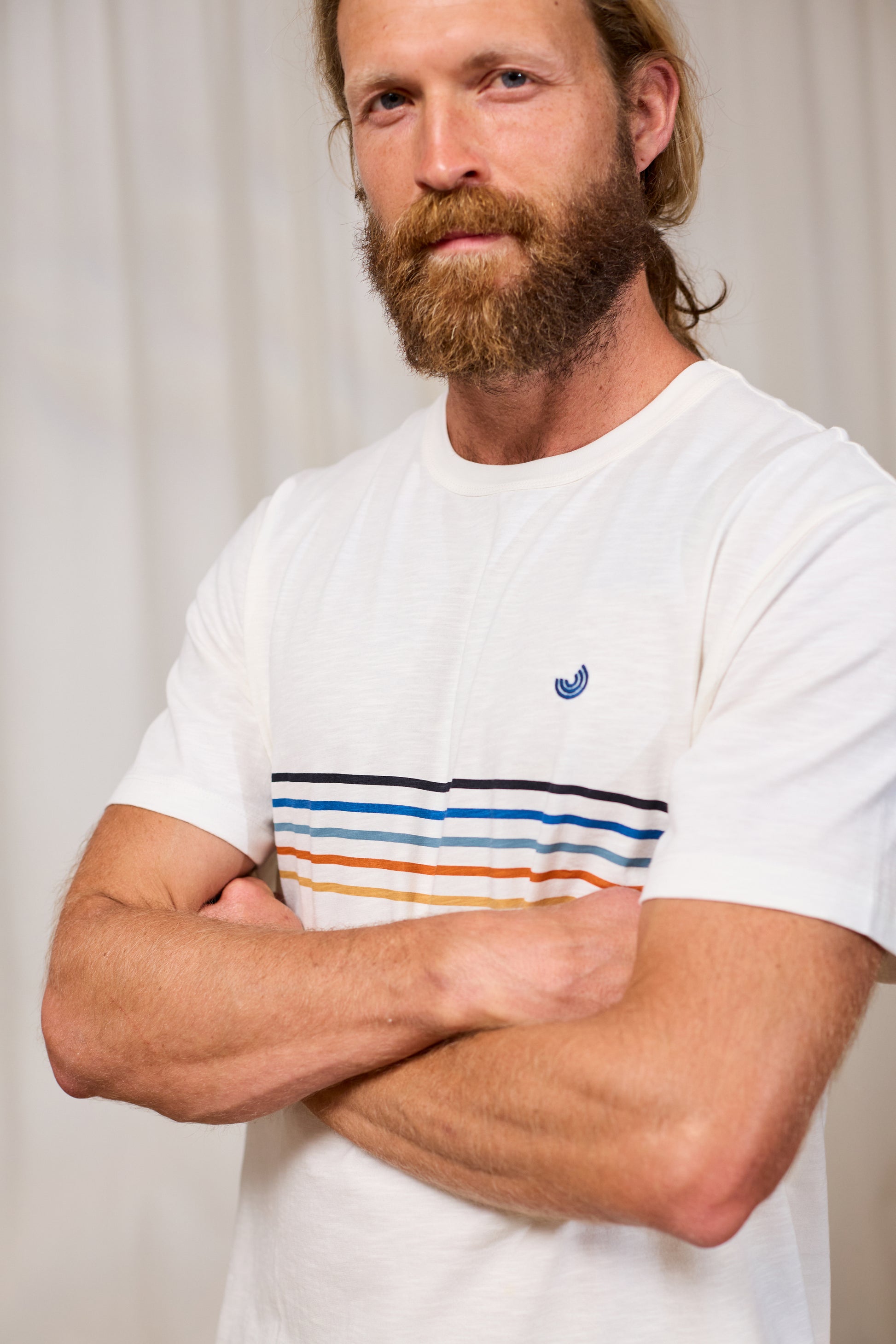 Man wearing a white organic cotton t-shirt with colourful stripes and TWOTHIRDS logo, standing against a plain background.