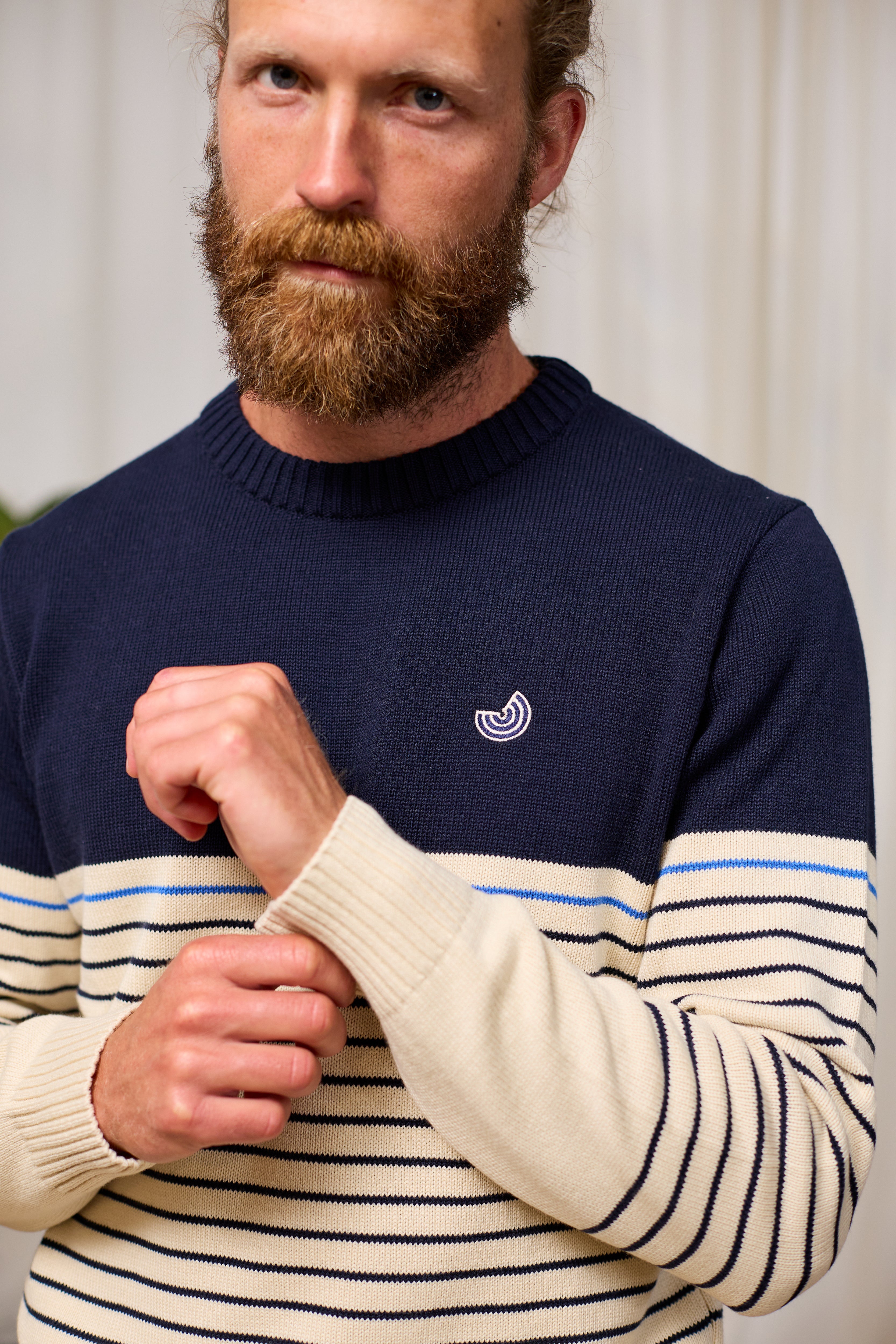 Man wearing a navy organic sweater with a white TWOTHIRDS logo and beige sleeves with black stripes.