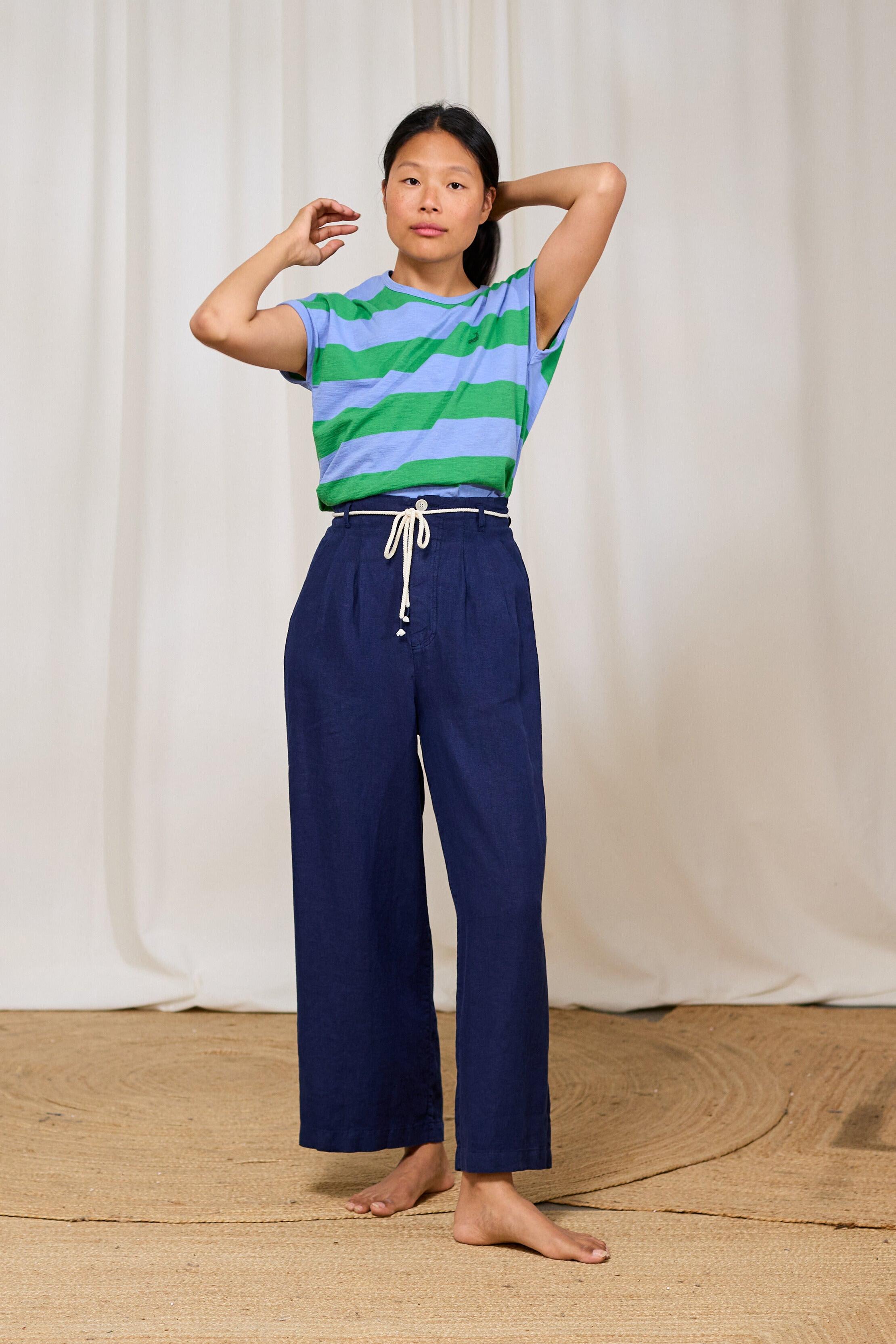 Model wearing a striped organic cotton shirt and blue pants against a white curtain background