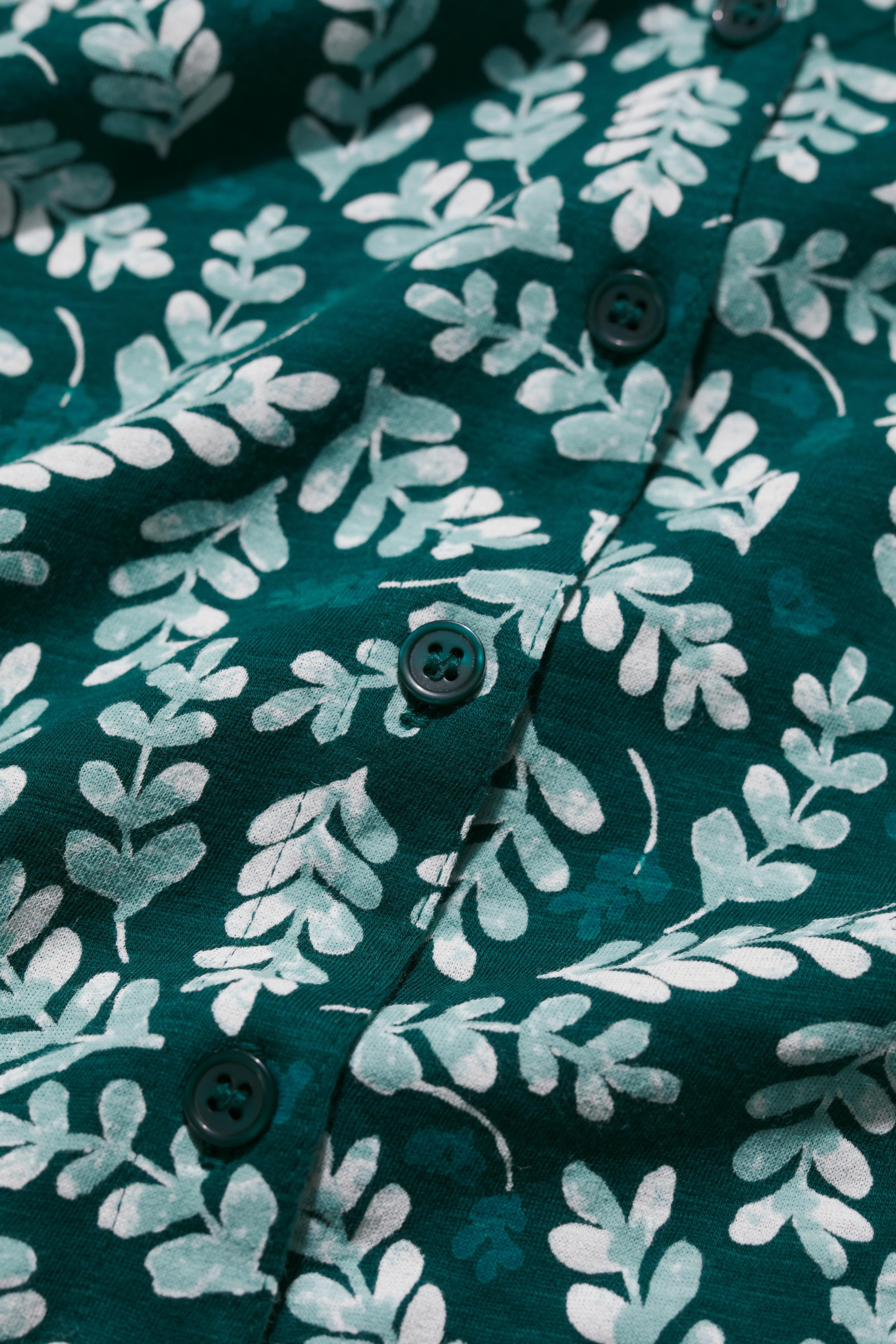 Close-up of a green organic cotton shirt with white leaf pattern and teal buttons.