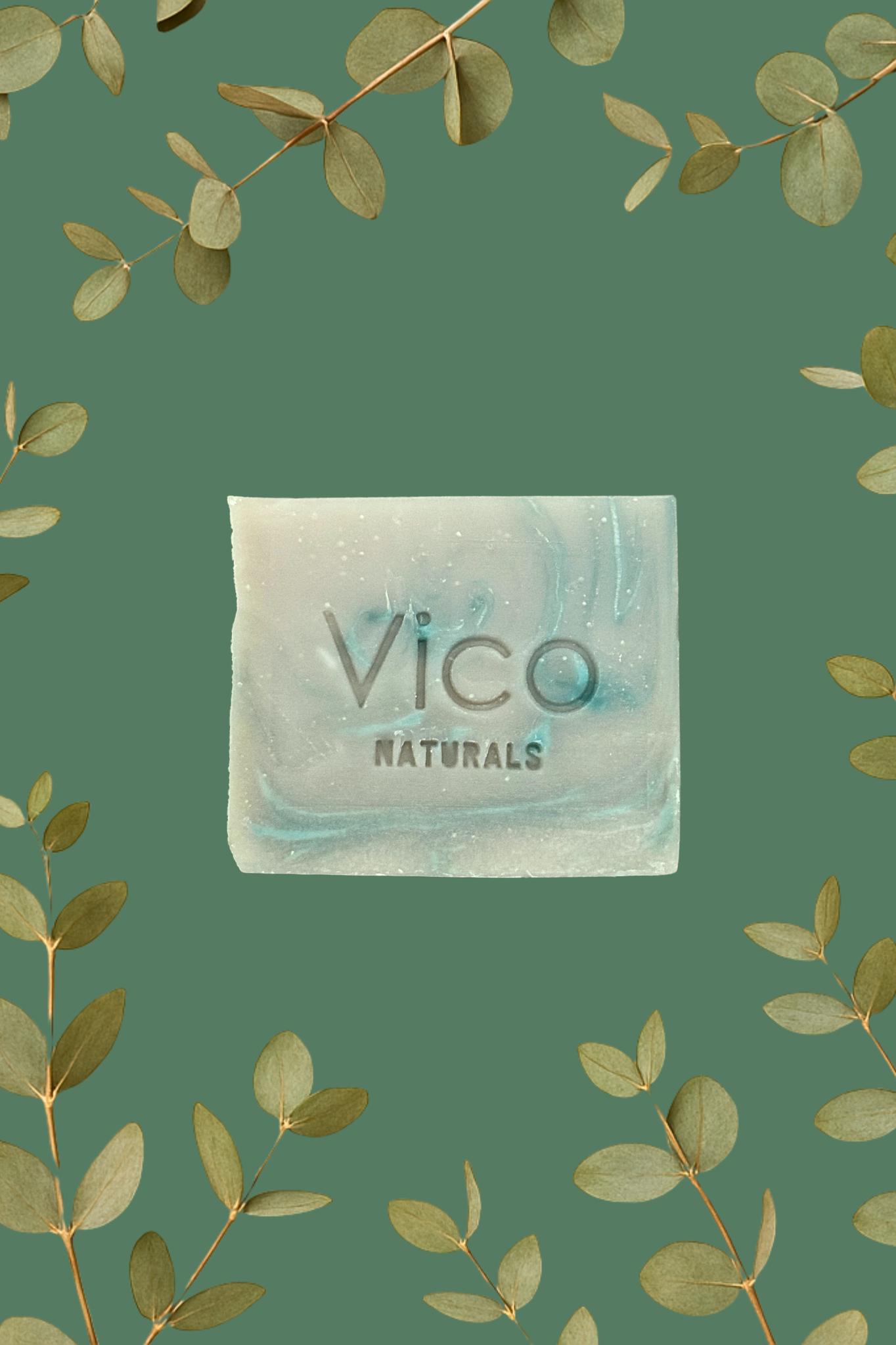 A square bar of Vico Naturals soap centered among a frame of eucalyptus branches on a green background.