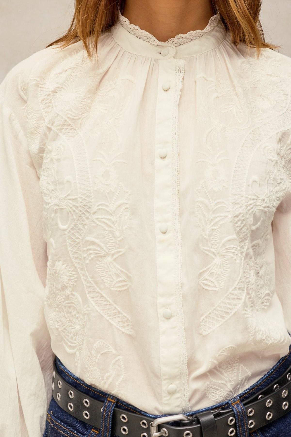 Woman wearing a white embroidered organic cotton blouse with a high neck and button-down front.
