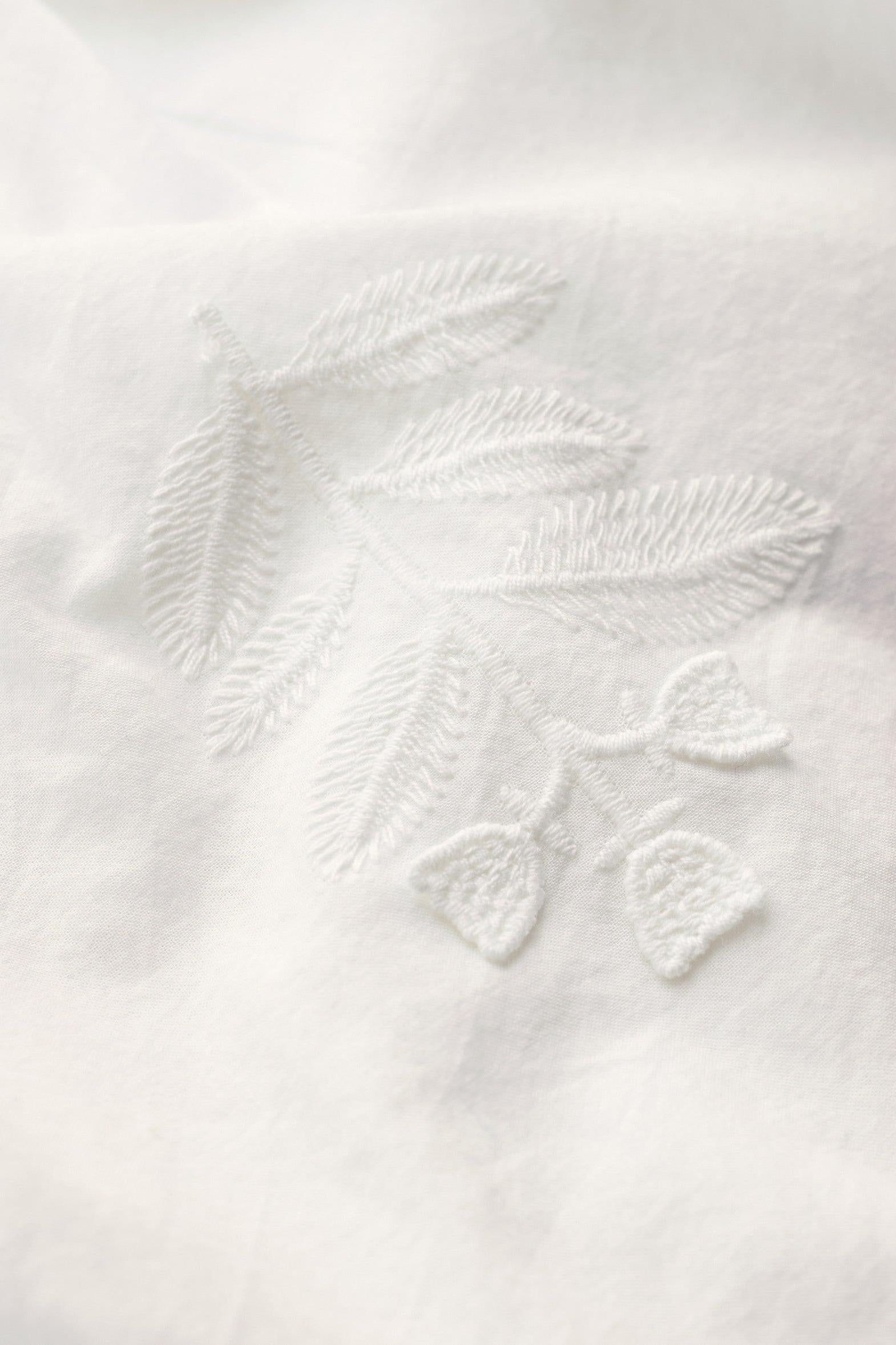 Close-up of white embroidered fabric with a delicate leaf motif stitched into a soft textile surface.
