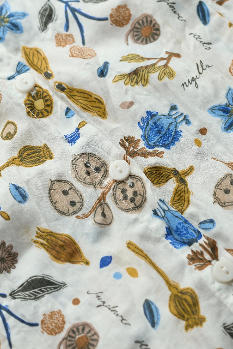 Close-up of a white Seasalt Cornwall cotton shirt featuring a botanical print with blue flowers and brown seeds.