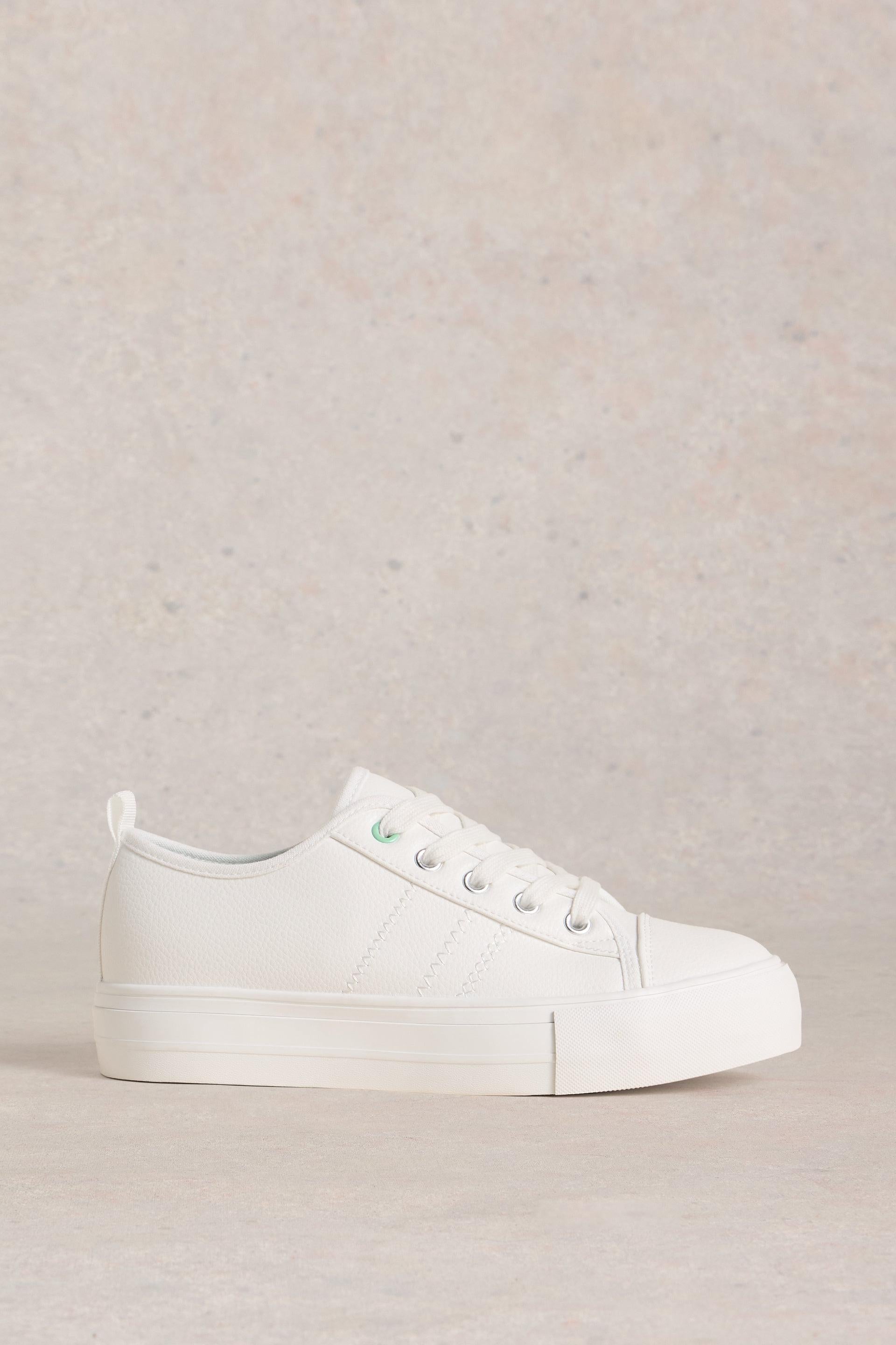 A minimalist white sneaker from White Stuff set against a neutral, textured background.