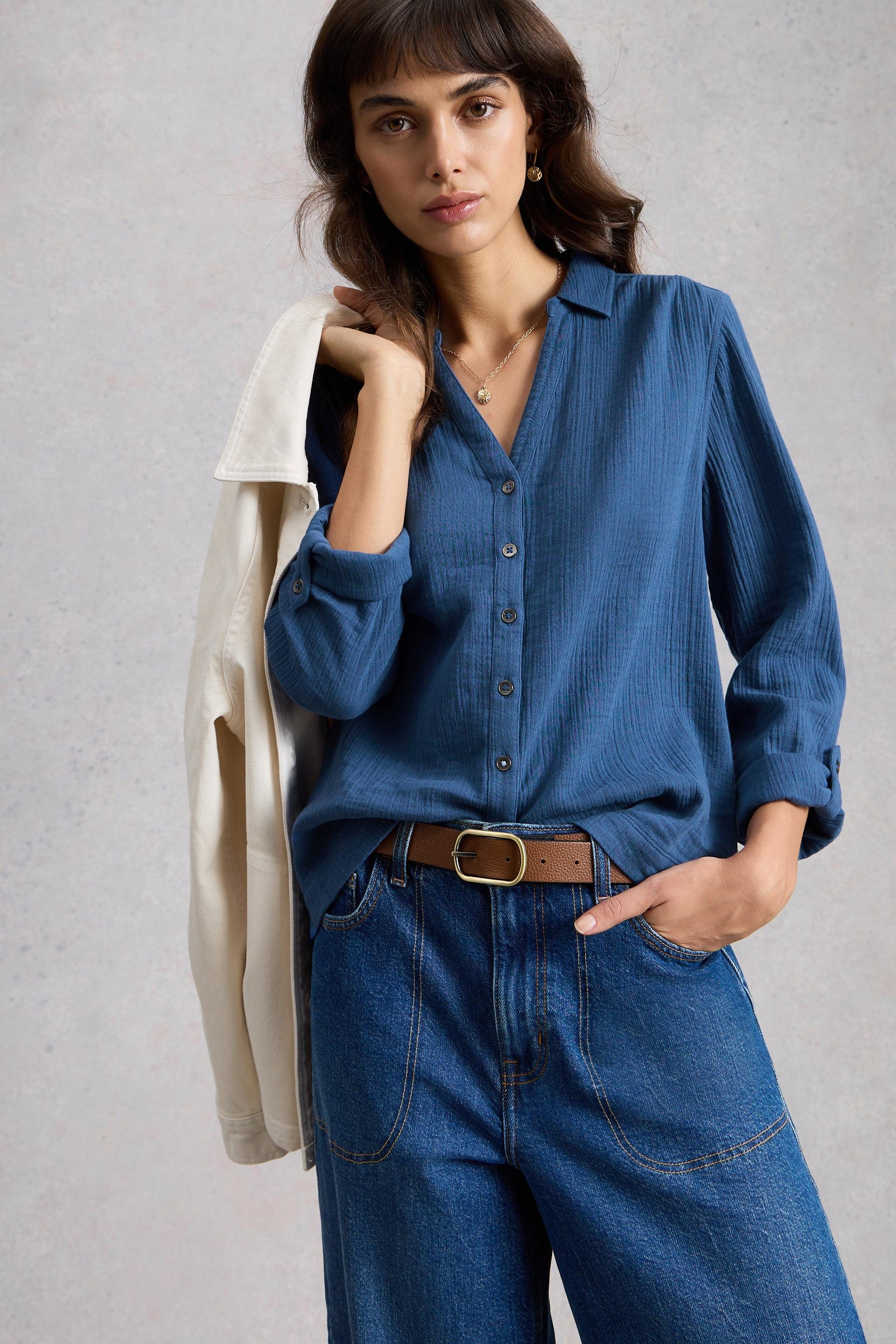 Woman wearing a blue organic cotton shirt and jeans against a gray background