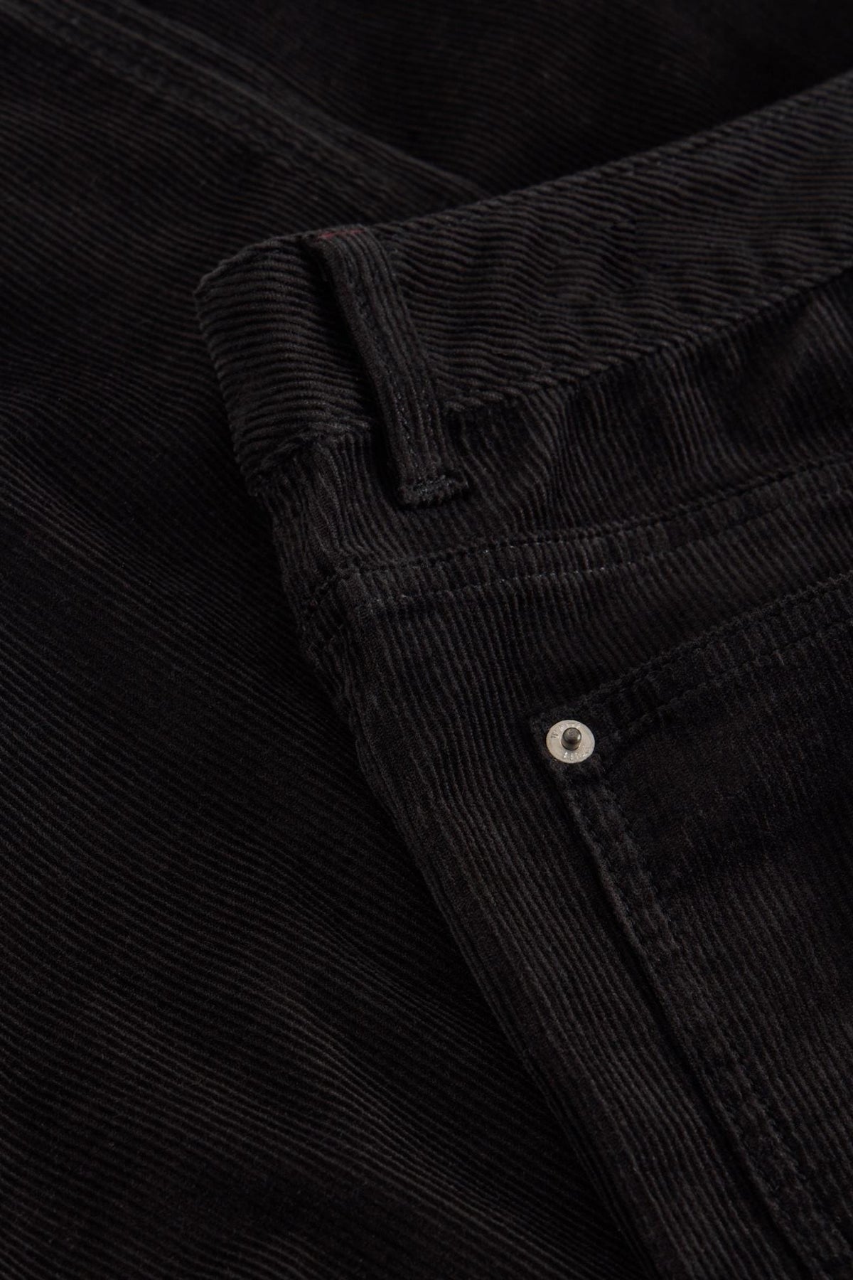 Close-up detail of black organic cotton corduroy trousers with metal rivet hardware.