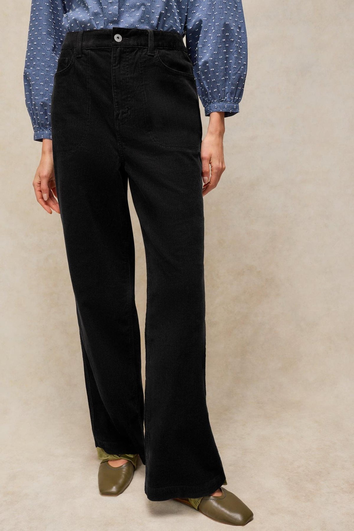 Woman wearing White Stuff black corduroy wide leg trousers with a blue polka dot blouse.