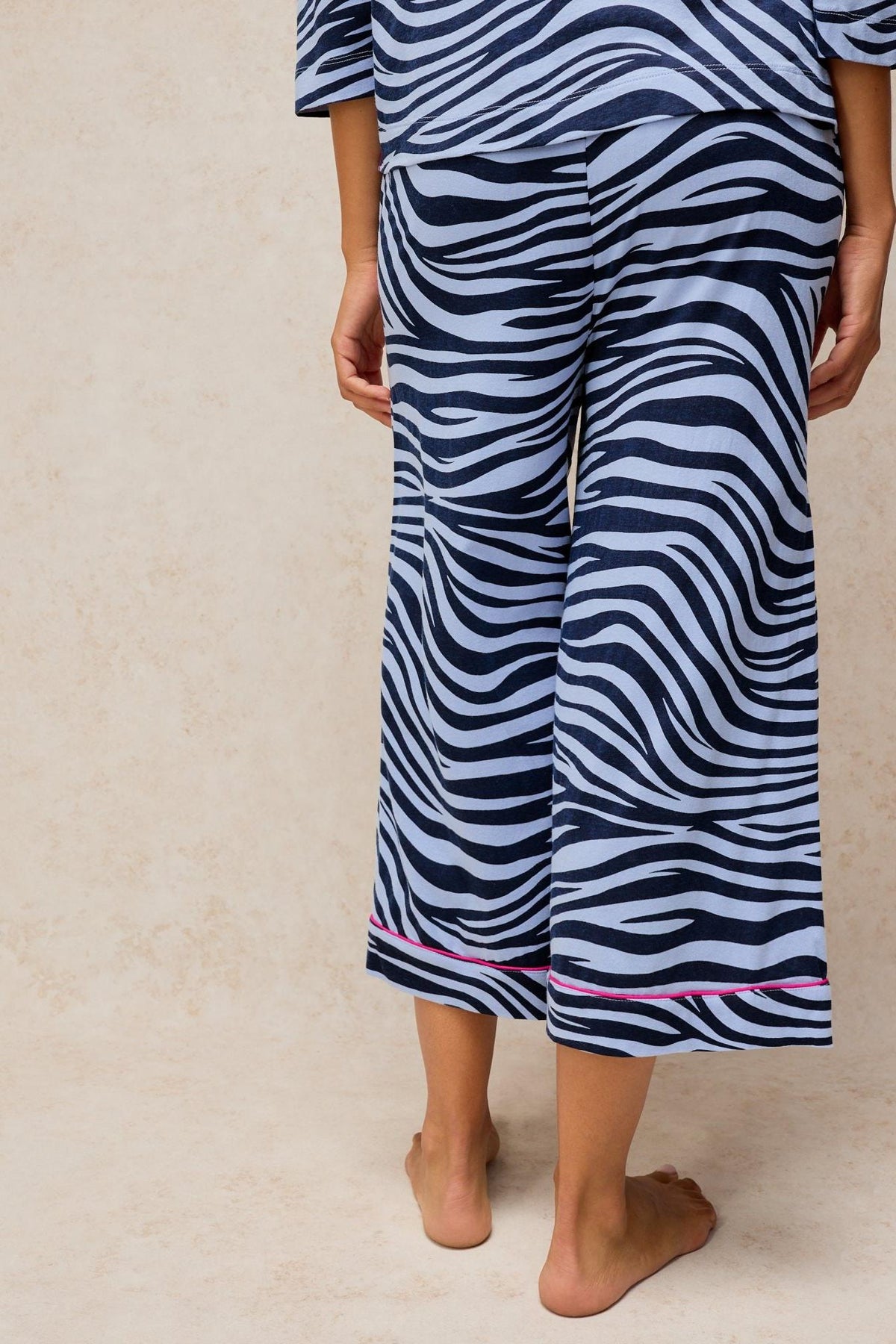 Woman wearing blue animal print cotton blend pyjama trousers from White Stuff against a neutral background.