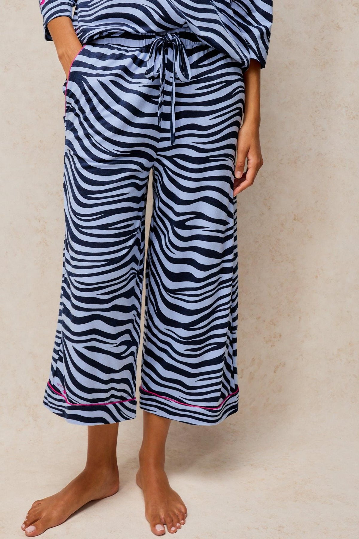 Person wearing blue animal print White Stuff pyjama trousers against a neutral background.