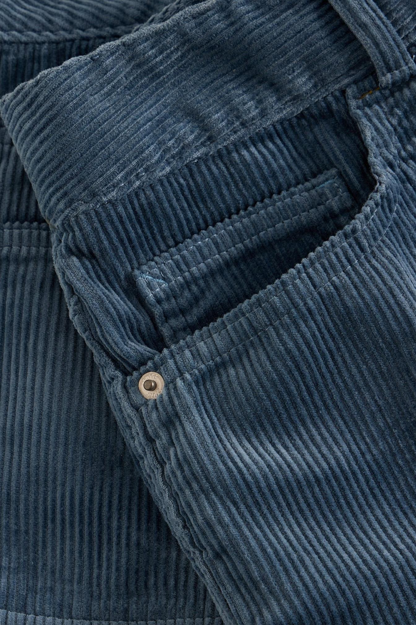 Close up of blue White Stuff cord trousers showing fabric texture and metal pocket rivet