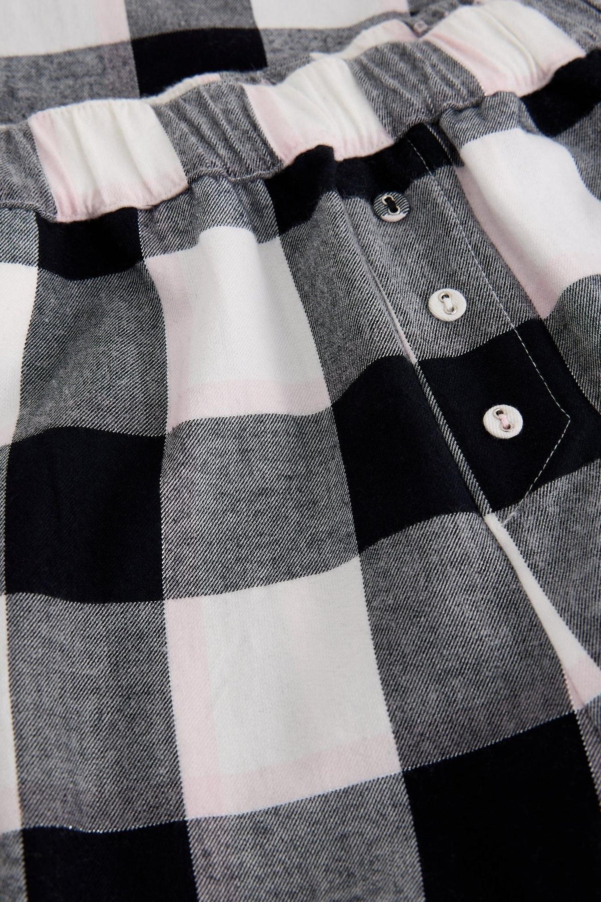 Close-up of White Stuff organic cotton pyjama bottoms featuring a black and white check pattern with button details.