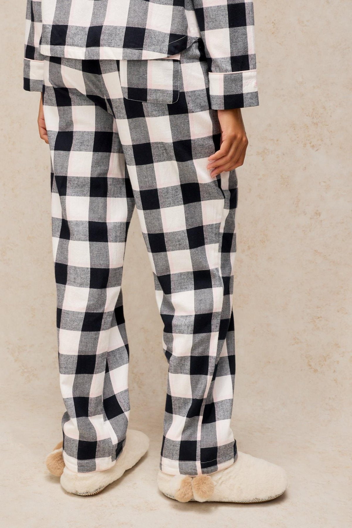 Rear view of a person wearing black and white check organic cotton pyjama bottoms and cosy slippers.