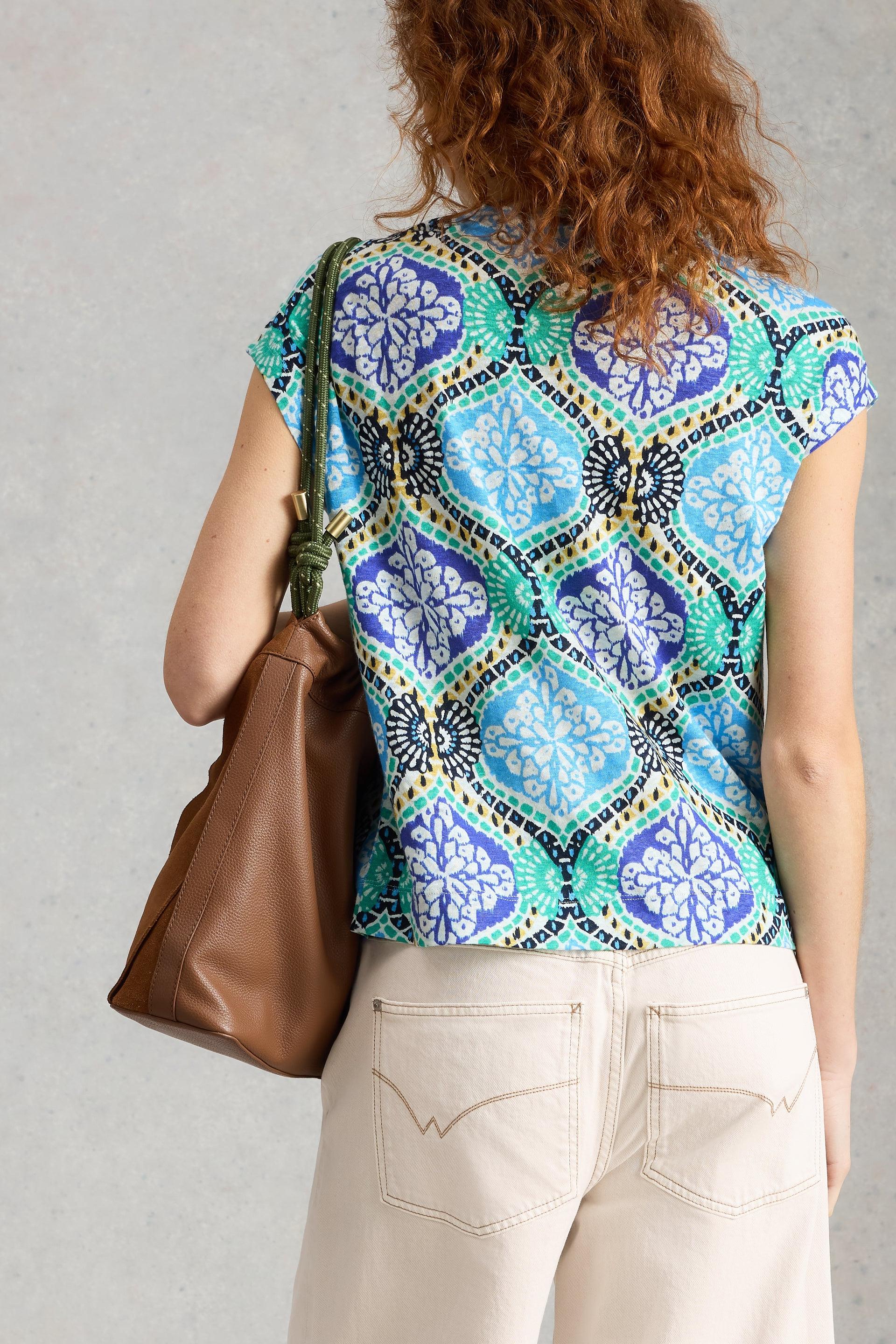 Person wearing a colourful linen top with a brown bag on a plain background