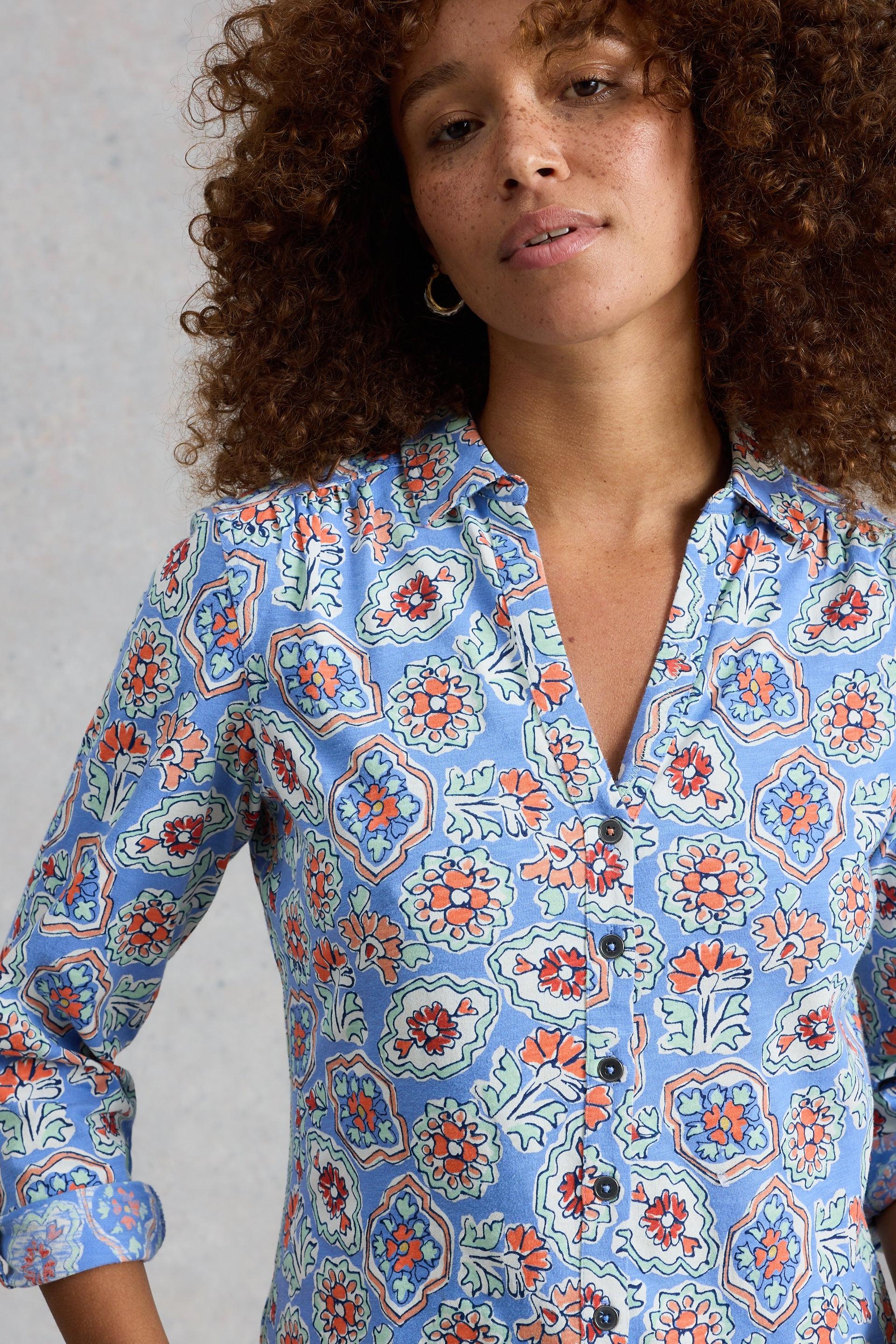Woman wearing a blue floral patterned shirt with collar, buttons and rolled sleeves.