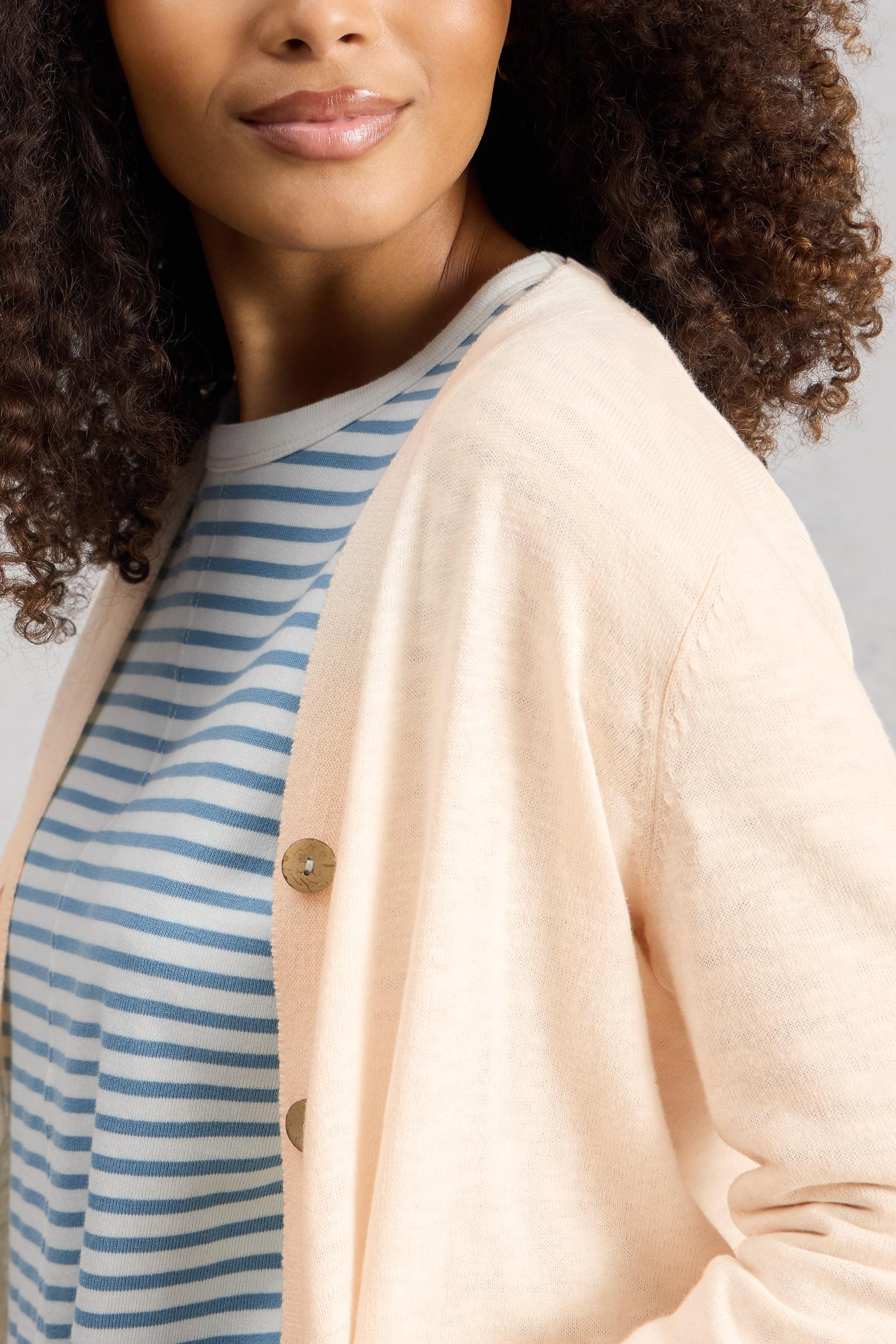 Woman wearing a cream organic cotton cardigan over a blue and white striped shirt against a gray background