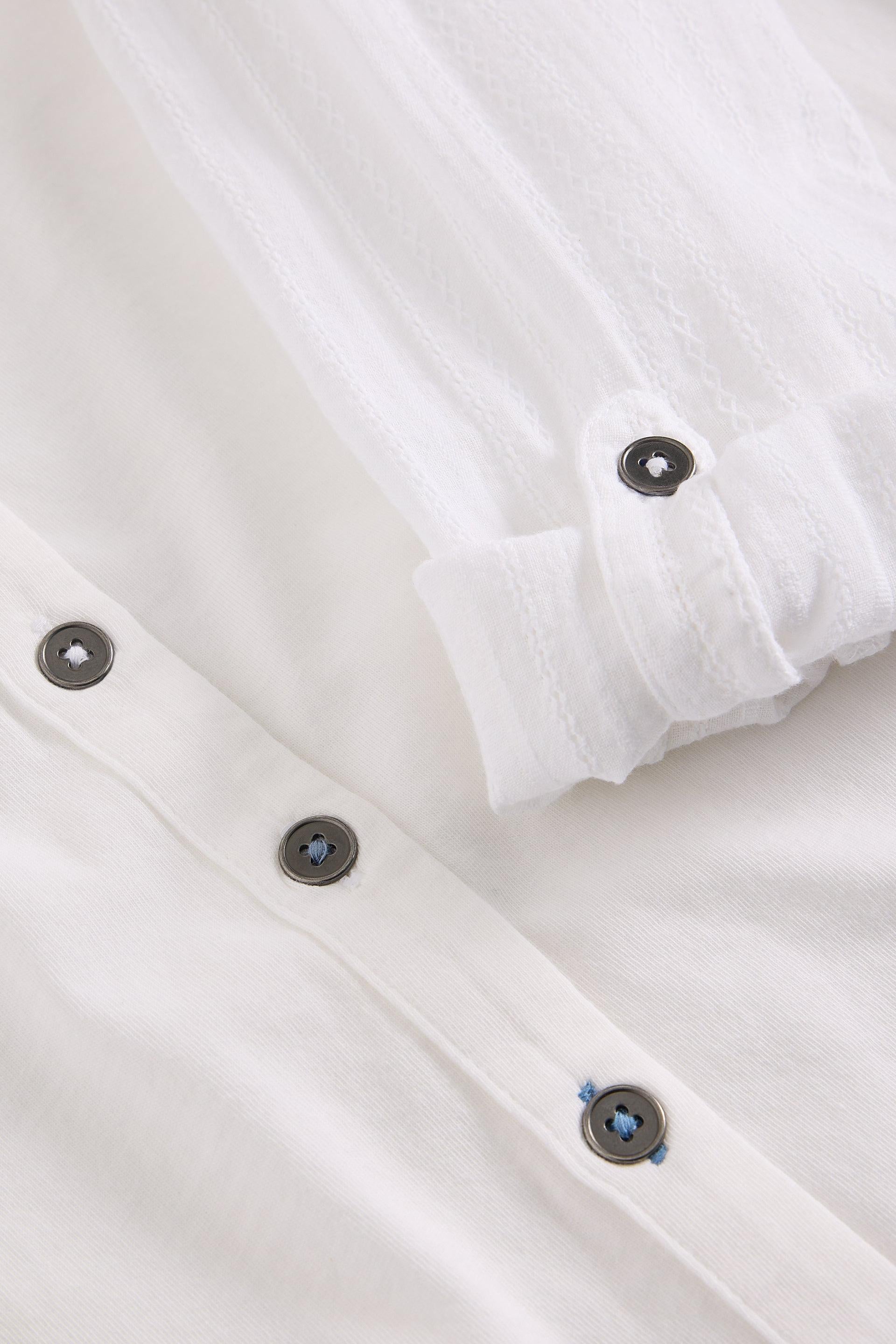 Close-up of a white cotton shirt with black buttons on a light background