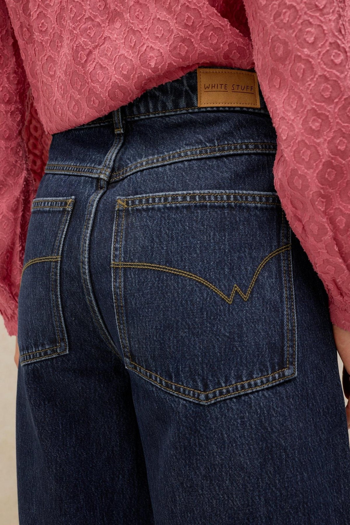Close-up of a woman wearing dark denim jeans from White Stuff with a pink textured blouse.