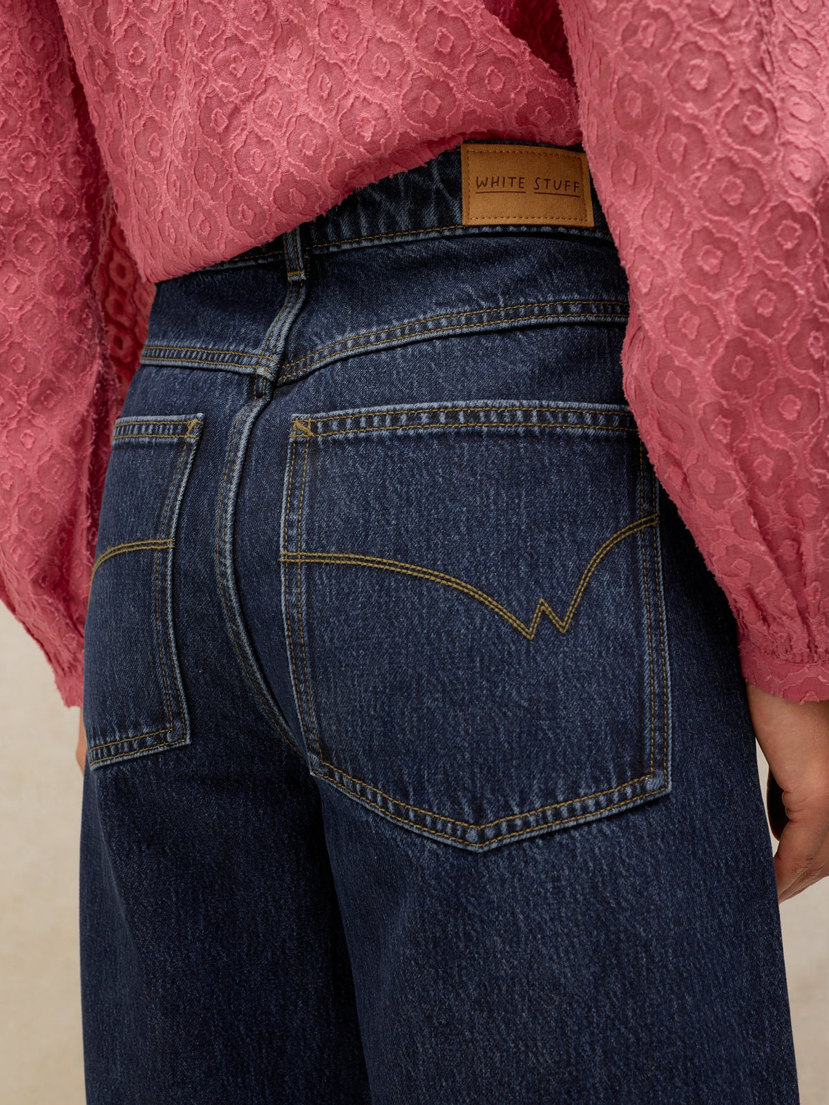 Close-up of a woman wearing dark denim jeans from White Stuff with a pink textured blouse.